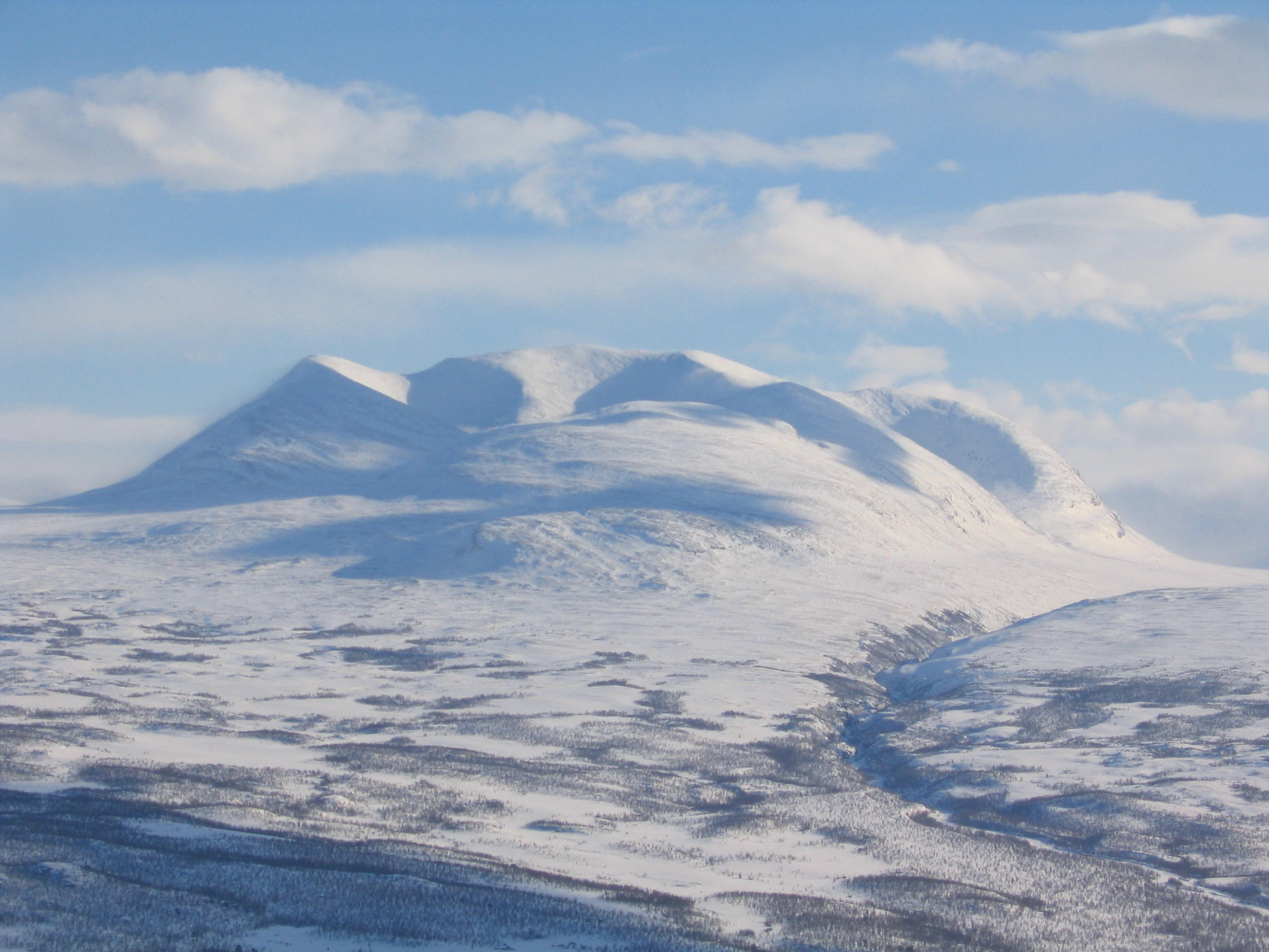 Snow-covered mountain range under a blue sky with scattered clouds