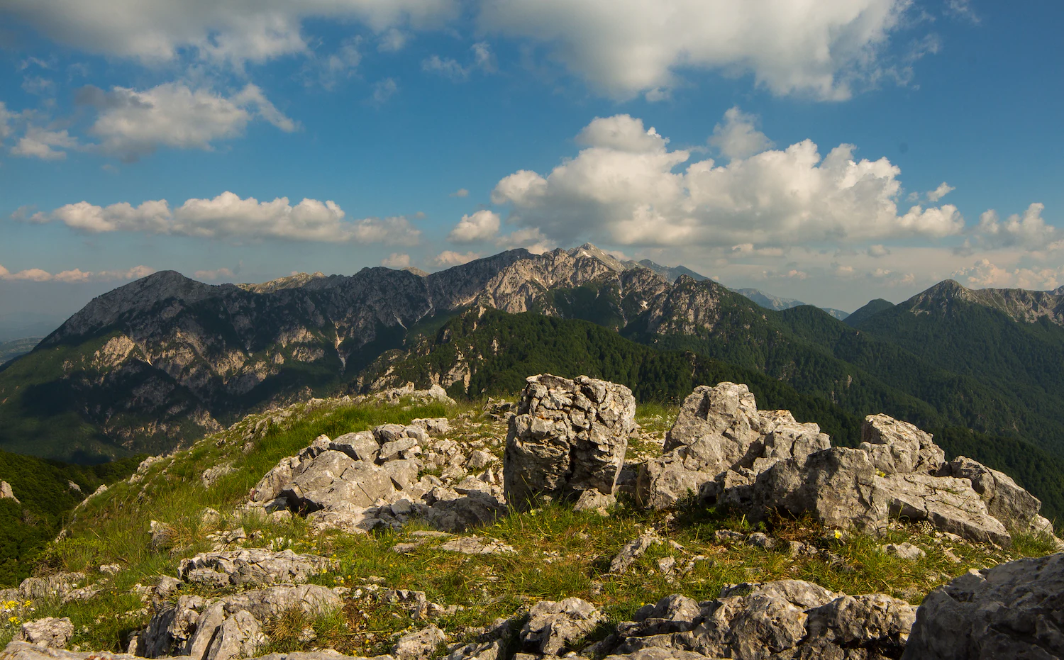 Mountain landscape with rocky outcrops in foreground and mountain peaks in background under a partly cloudy sky