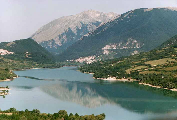 A large lake surrounded by mountains with green hills and a small town in the distance