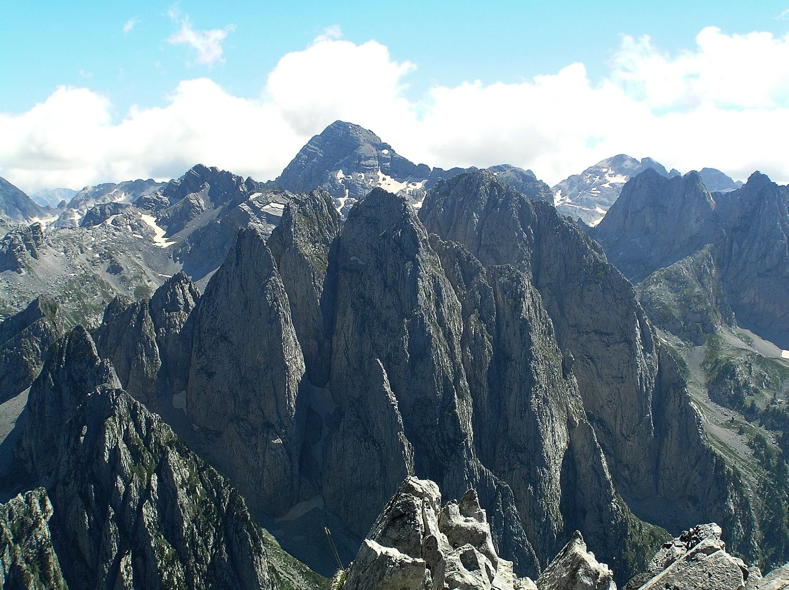 A wide, eye-level view of a jagged mountain range with dark, rocky peaks and patches of snow, seen from a high vantage point.