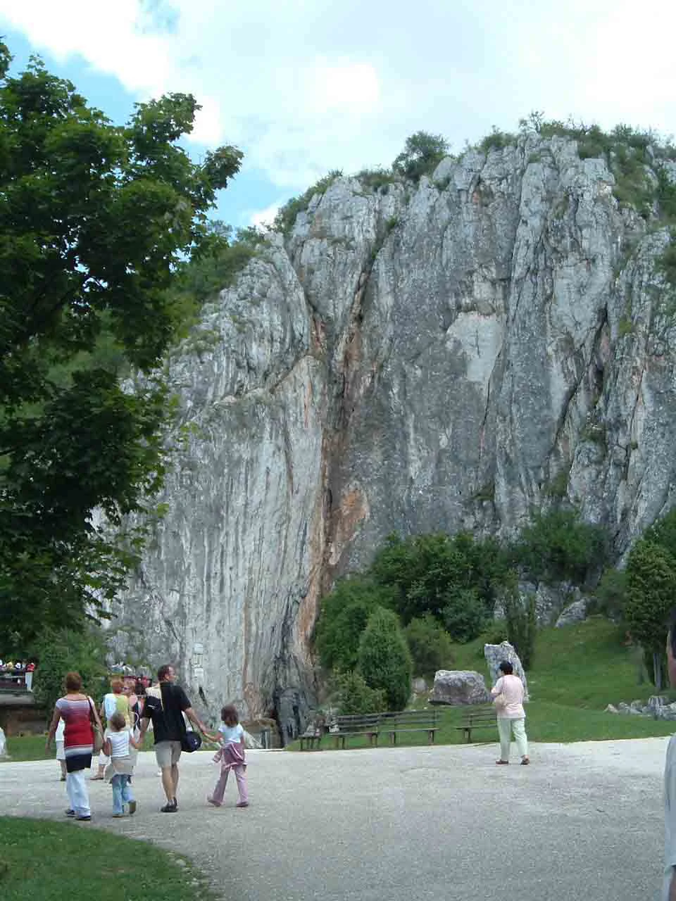 People walking toward a large rocky cliff face with a cave entrance visible