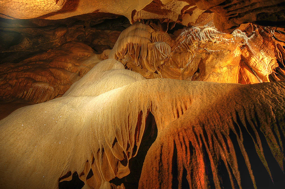 Close-up view of orange and white stalactites hanging from a cave ceiling with layered rock formations