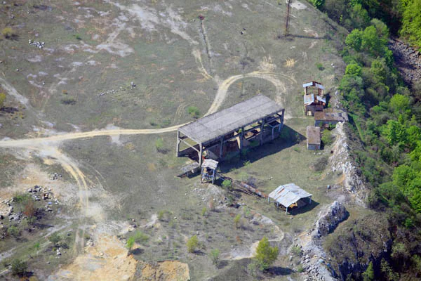 Aerial view showing an open-sided structure and smaller buildings on rocky terrain with dirt paths and sparse vegetation