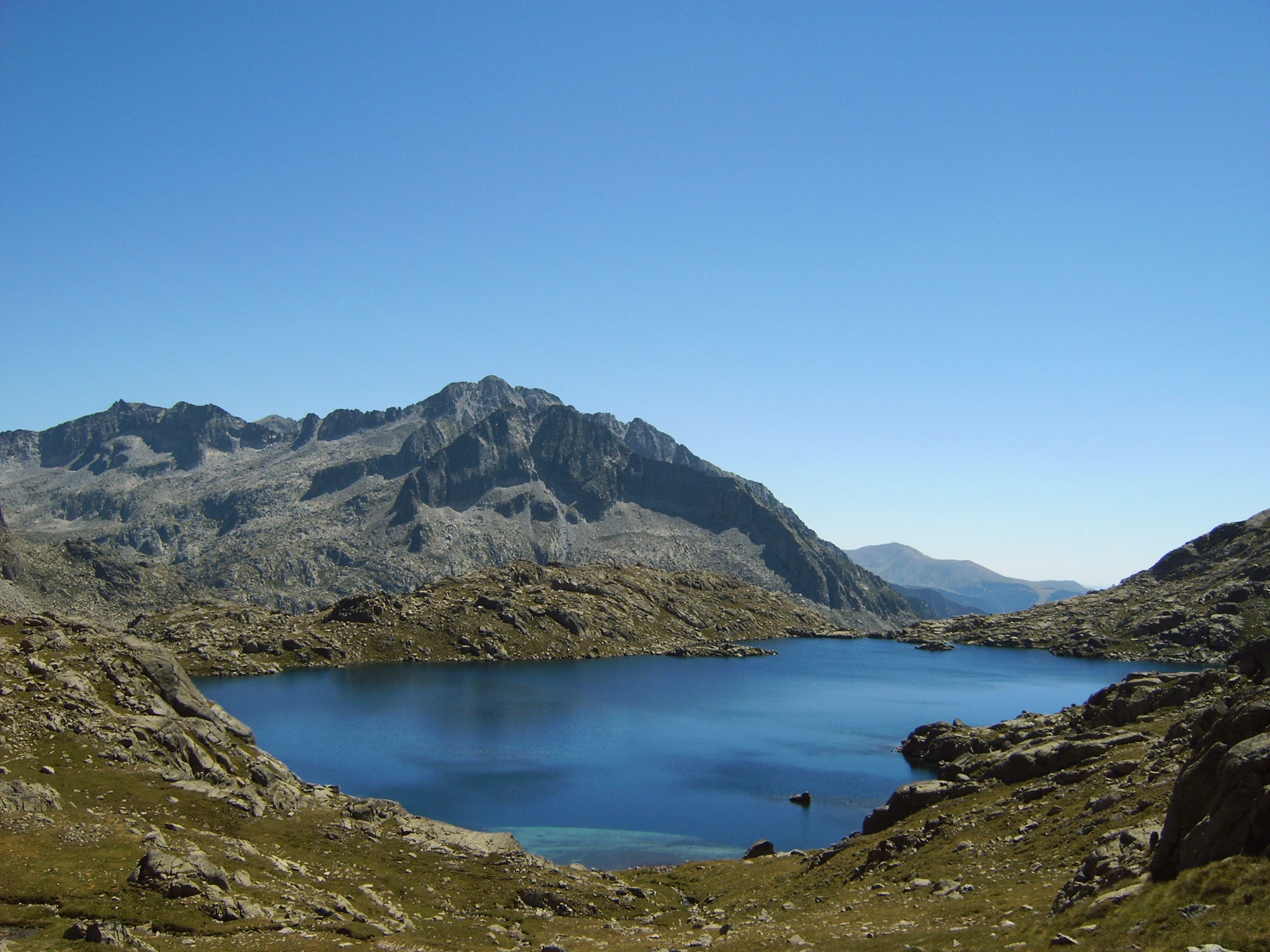 A clear blue lake surrounded by rocky mountain slopes under a bright blue sky