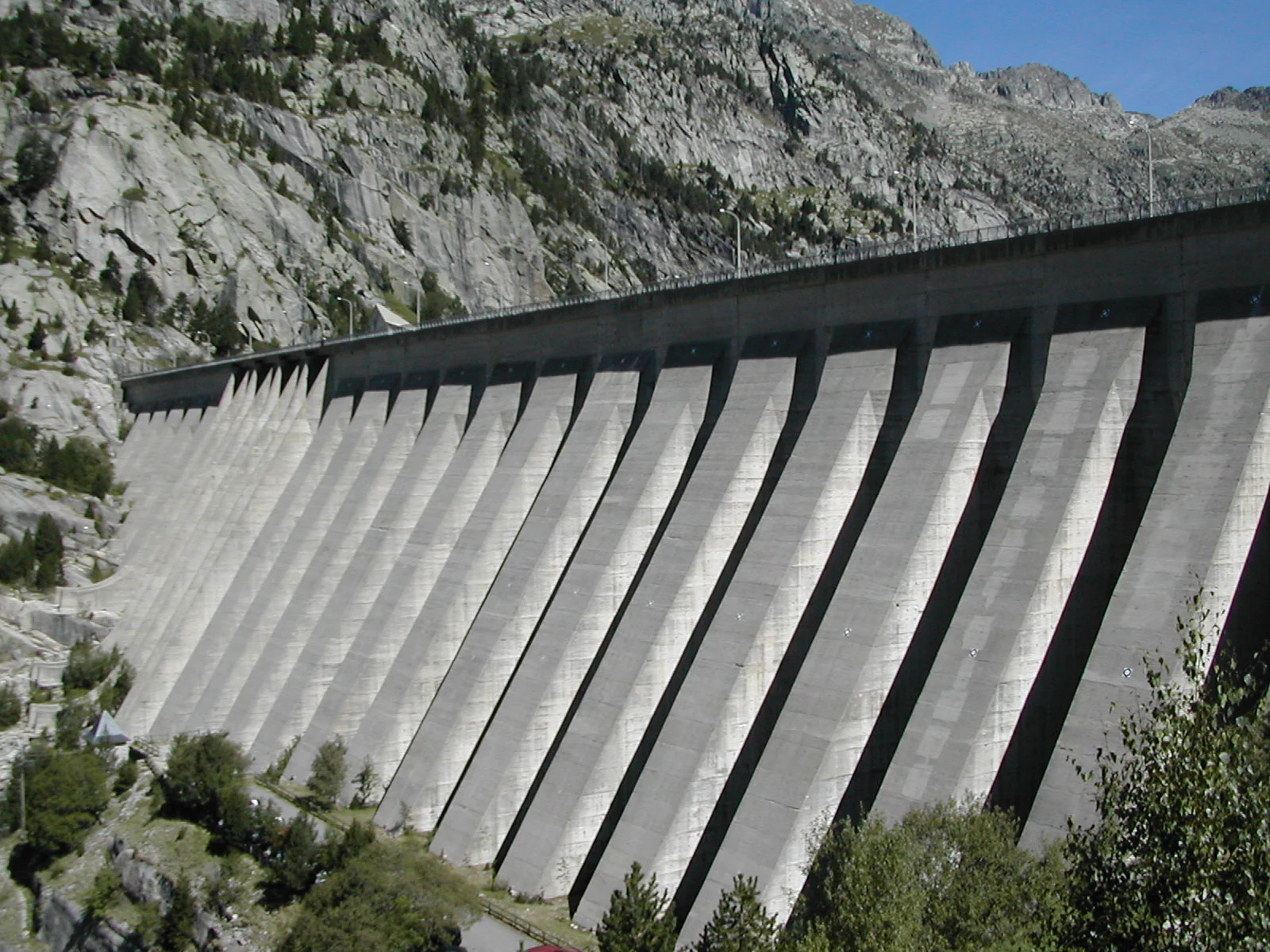 Concrete dam with multiple spillway sections in a mountainous landscape with trees