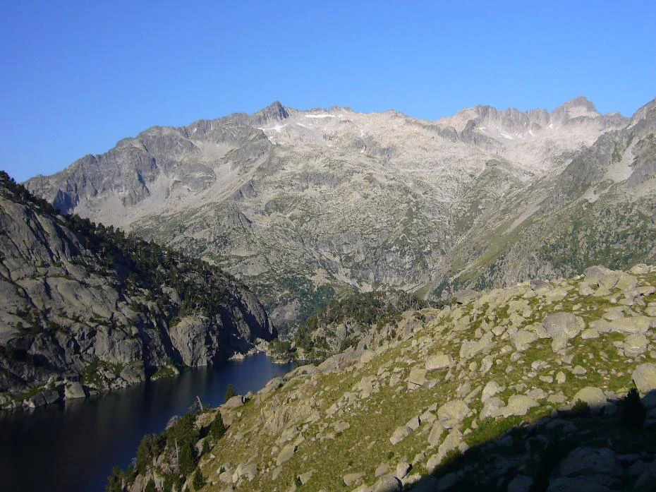 Mountain lake landscape with rocky slopes and snow-capped peaks under a clear blue sky