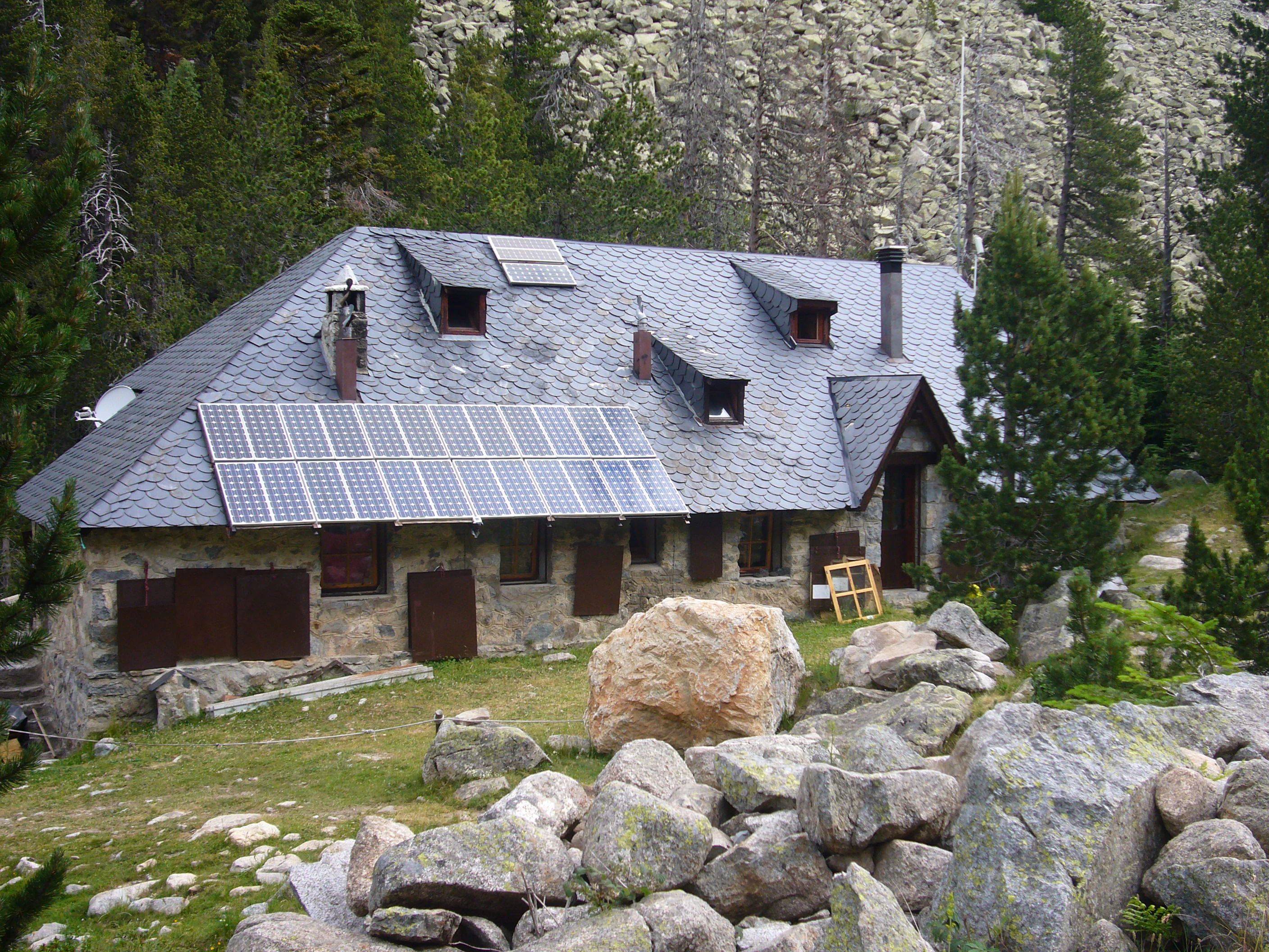 Stone building with slate roof and solar panels surrounded by rocks and forest in a mountainous area