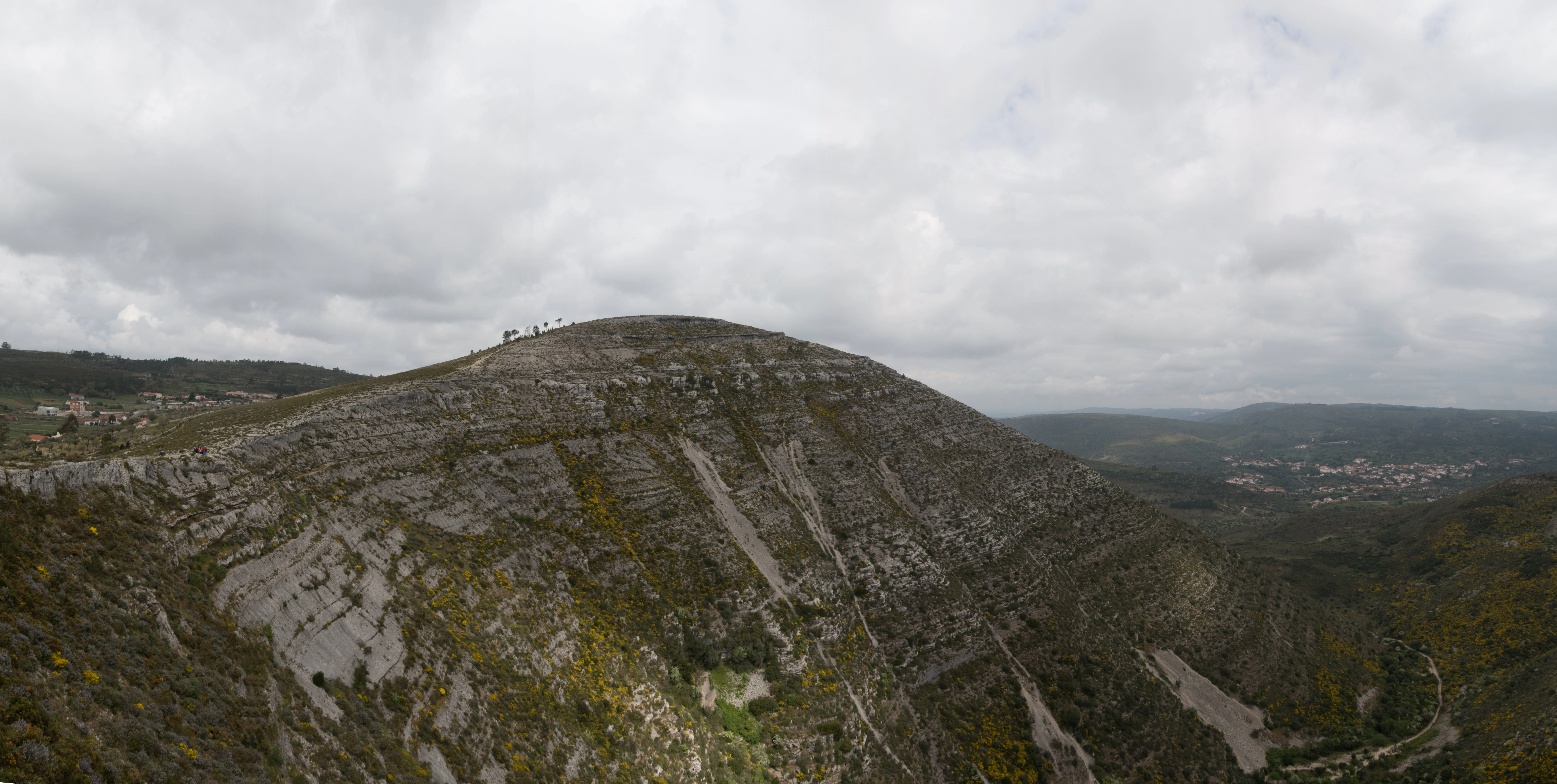 Wide landscape view of exposed limestone hills under a cloudy sky with distant valleys