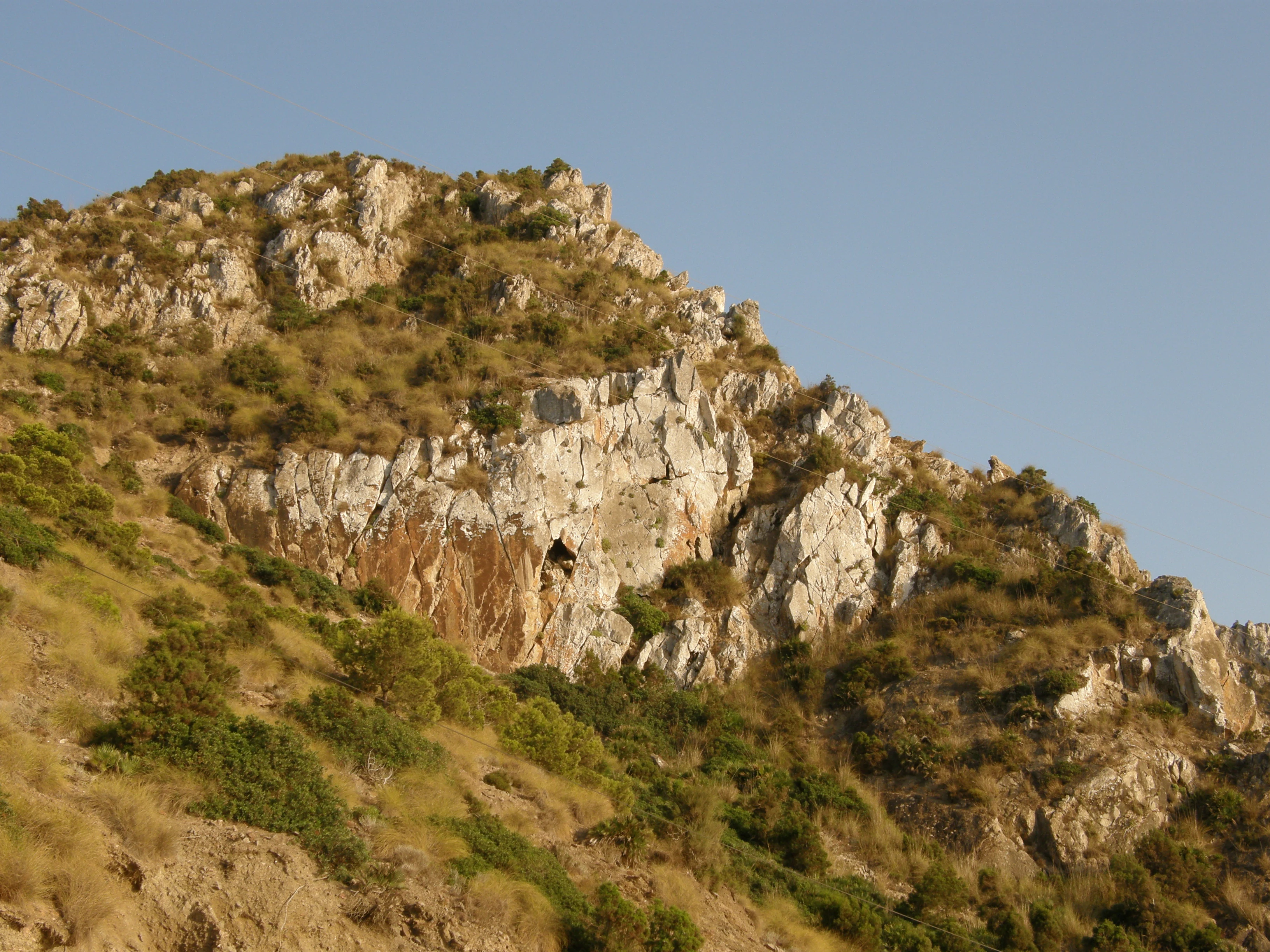 Rocky mountain cliffs with sparse vegetation under a clear blue sky