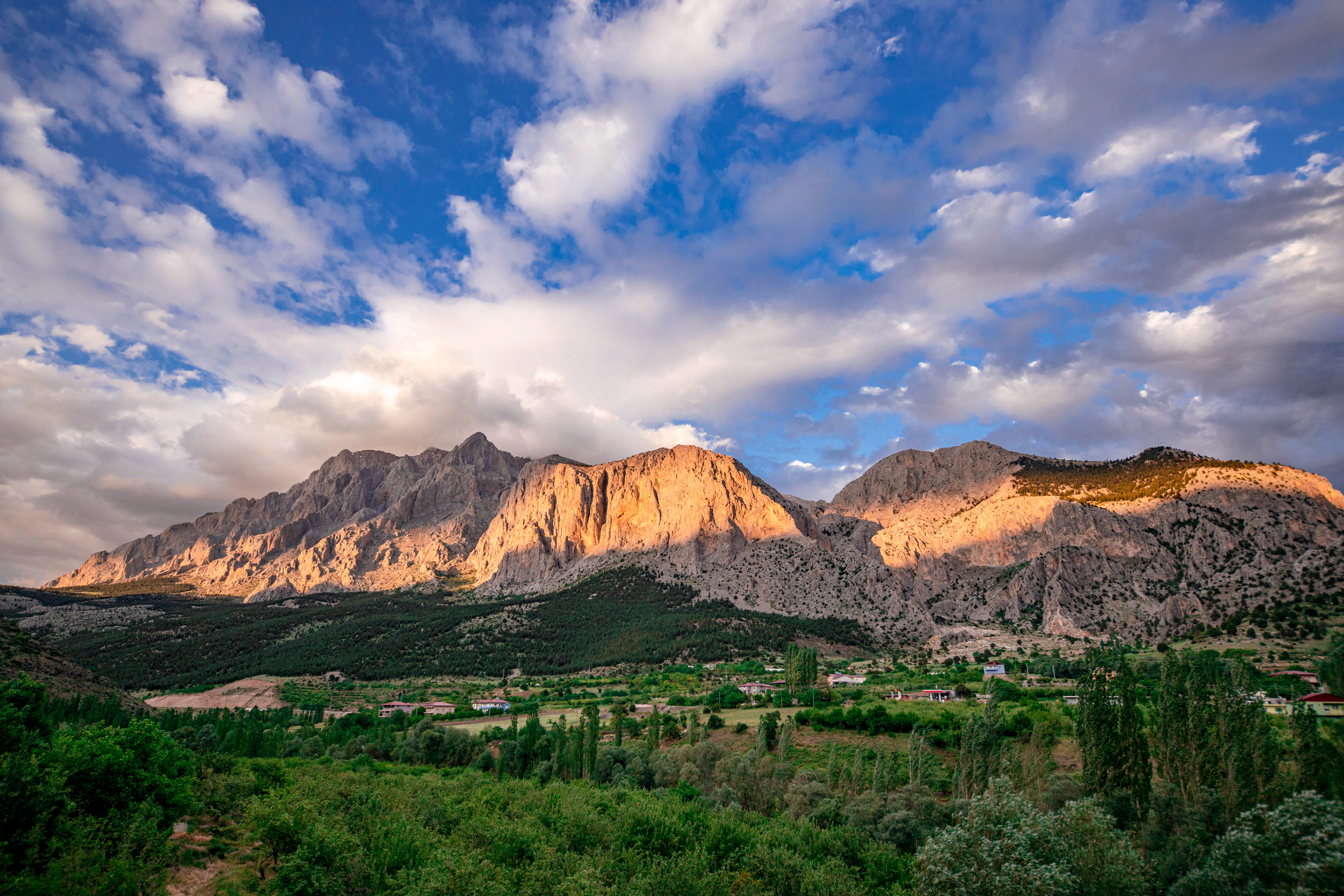 Landscape view of Yelatan Village in Aladağlar National Park featuring mountain peaks, green valley, and blue sky with scattered clouds