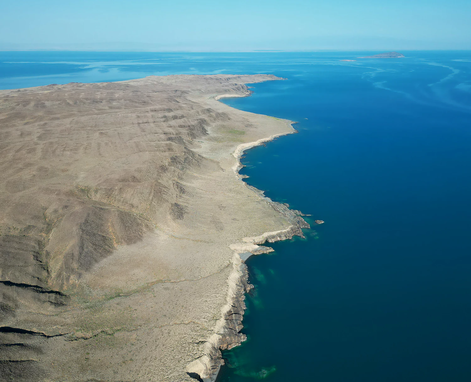 An aerial view of large, arid islands surrounded by deep blue lake water, showcasing a rugged coastline and rocky terrain.