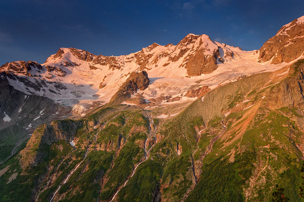 Snow-covered mountain peaks with green valleys under a clear blue sky