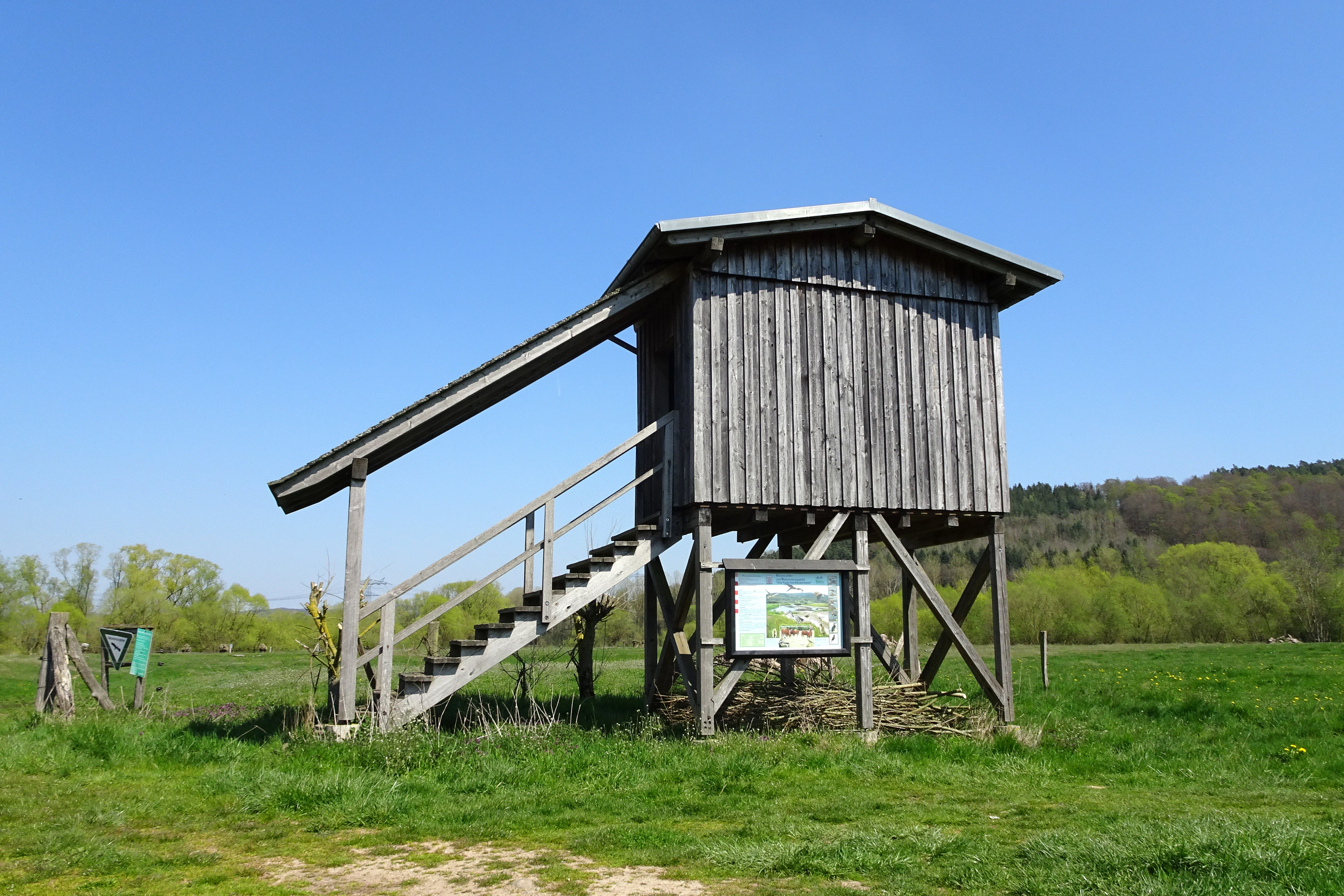 A raised wooden observation tower standing in a grassy meadow with a clear blue sky above.