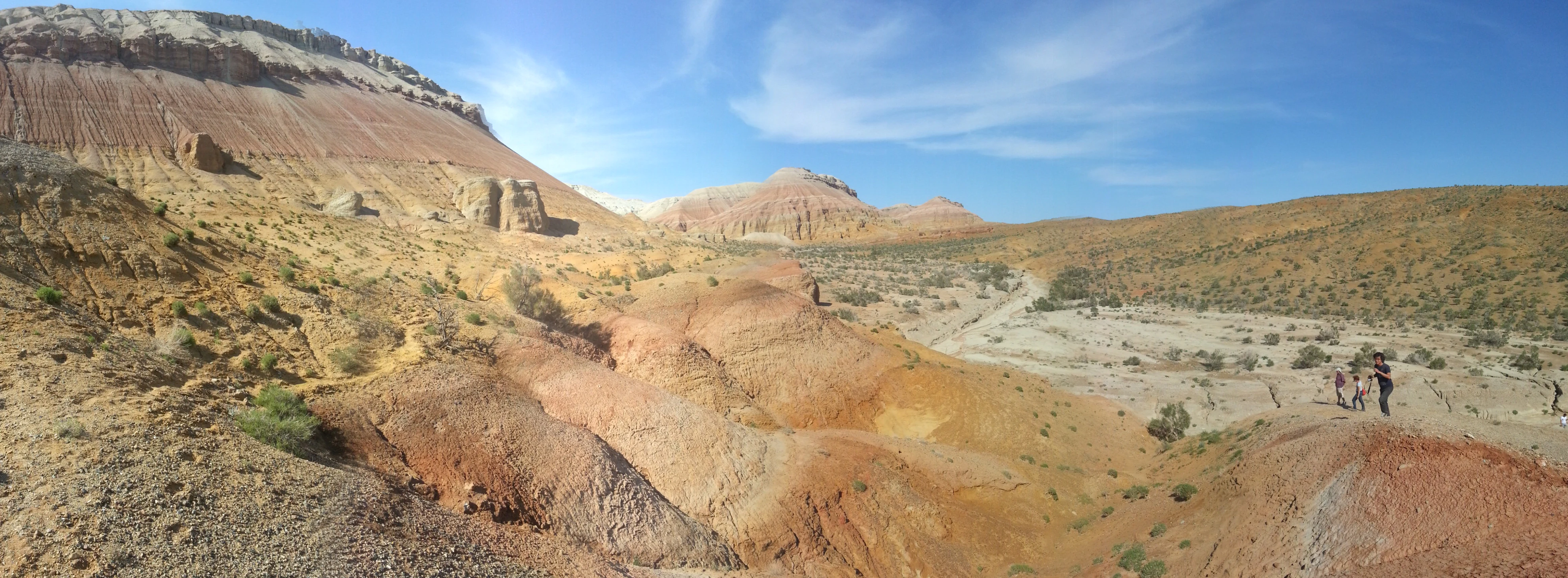 Panoramic view of reddish-brown Aktau mountain rock formations with sparse vegetation under a clear blue sky