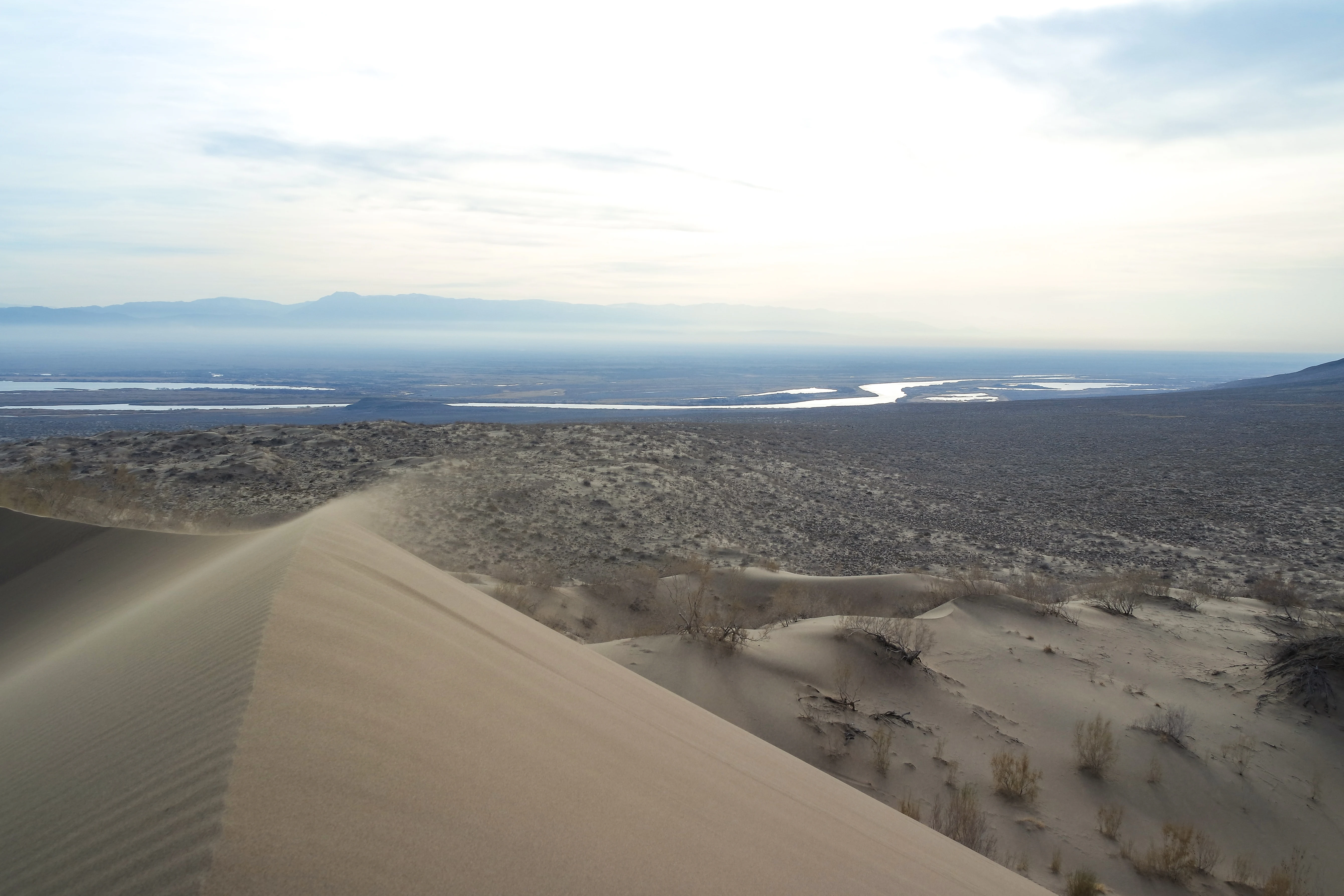 Sand dunes with a river and mountains in the background, part of Altyn-Emel National Park