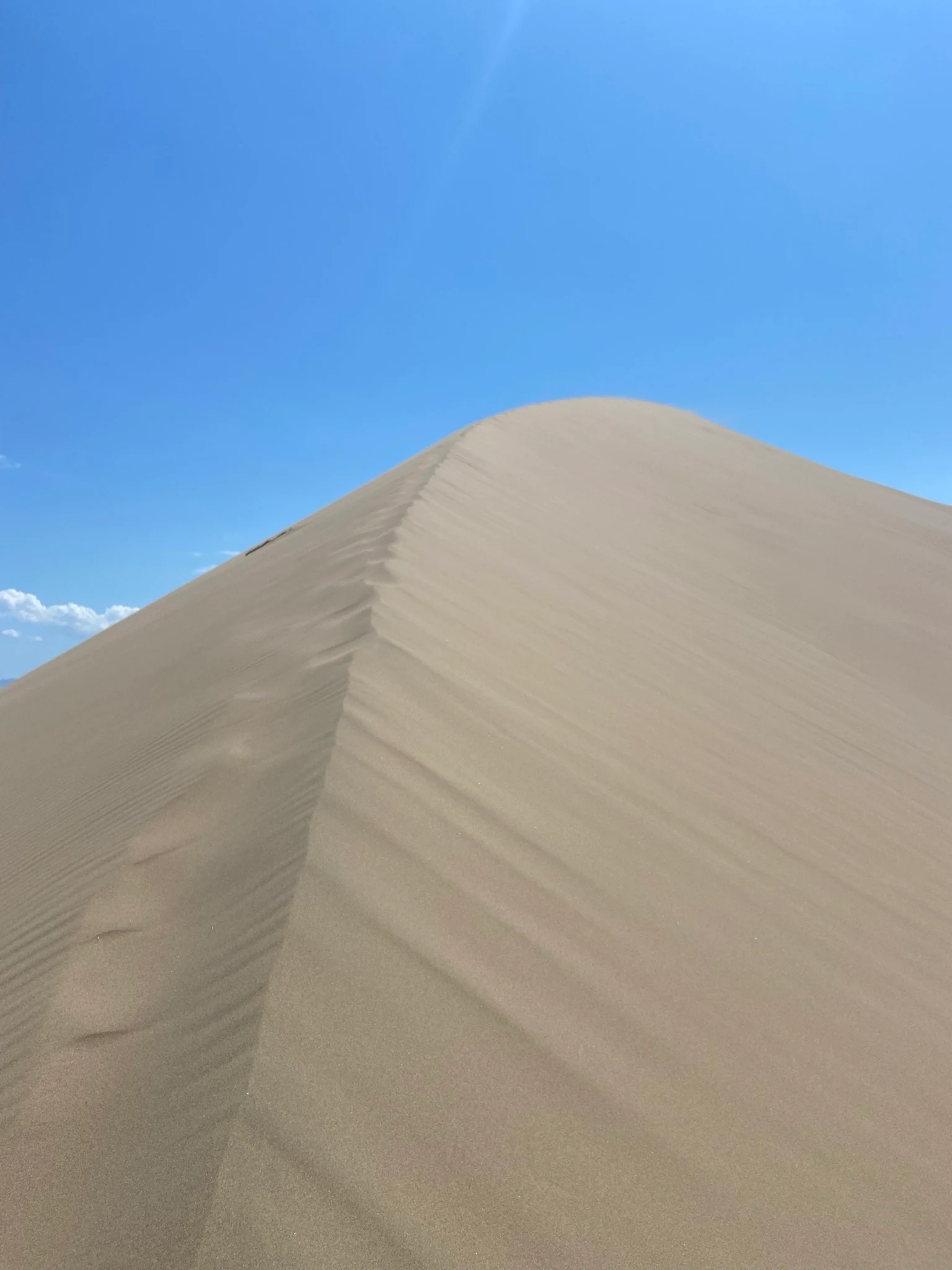 Large sand dune with visible wind-formed ridges under a clear blue sky