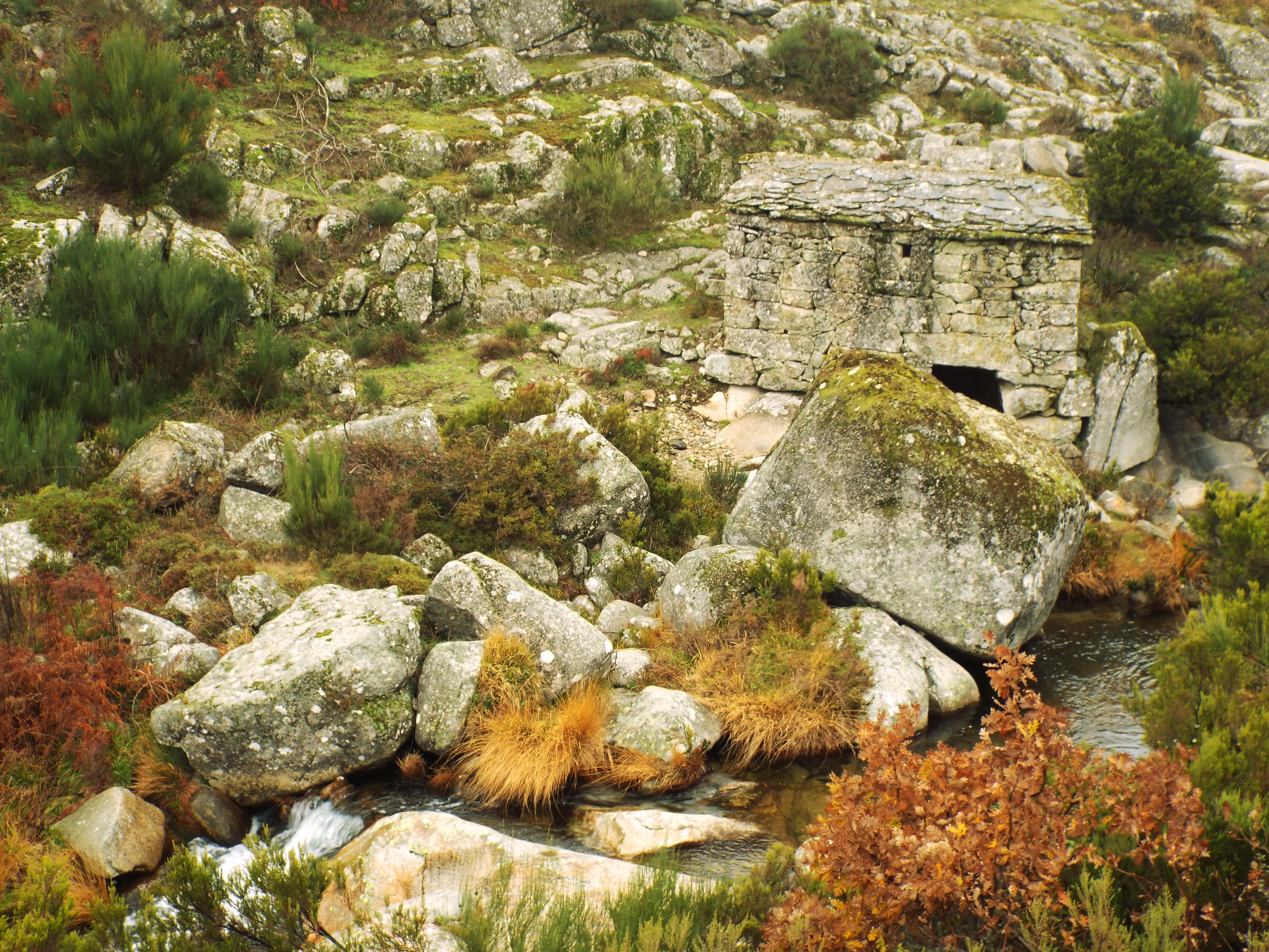 Stone building ruins on rocky terrain with stream and vegetation