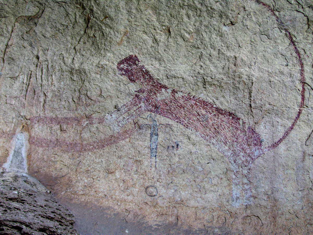 A reddish-brown, long-tailed panther pictograph painted on a weathered, rough limestone rock surface.