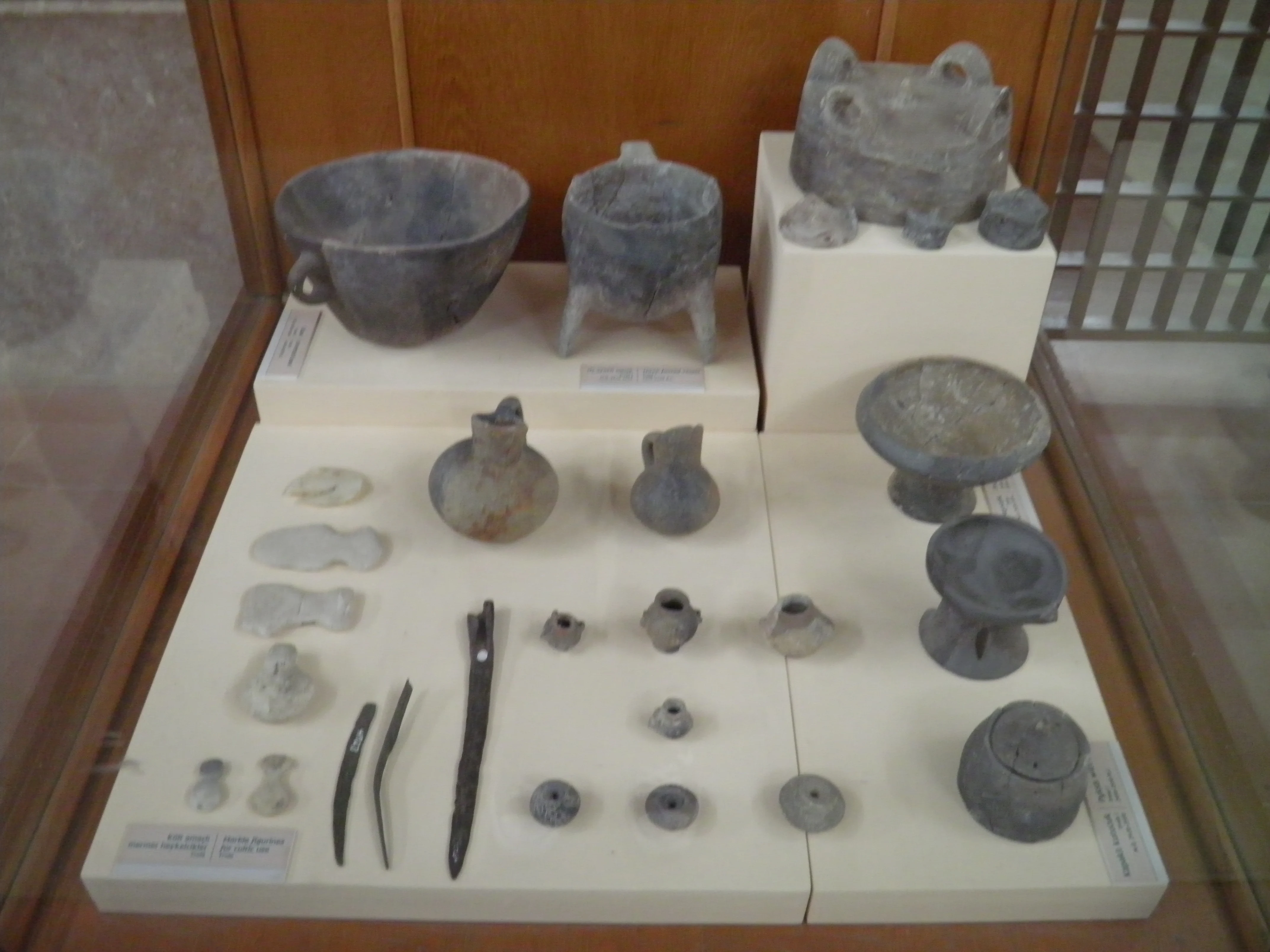 Museum display case containing ancient pottery vessels, stone tools, and small sculptures