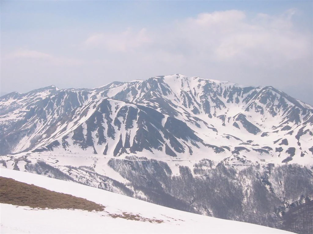 Snow-covered mountain peaks with rocky ridges under a partly cloudy sky