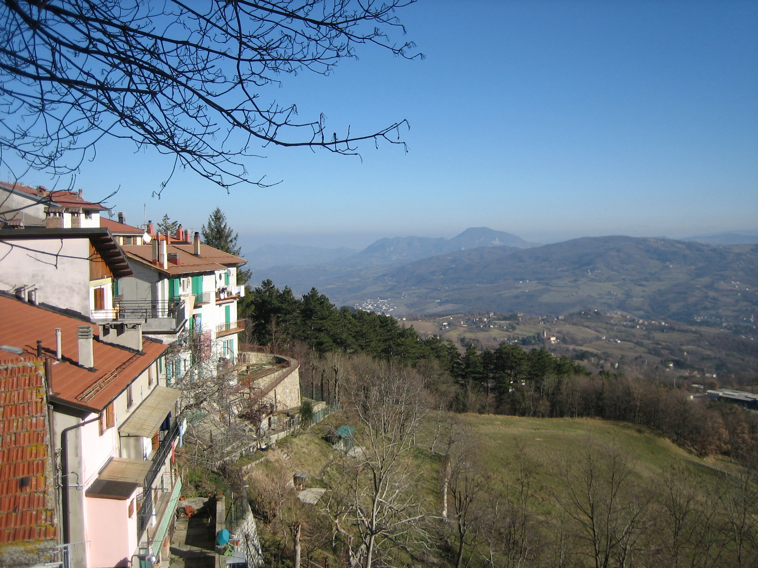 Red-tiled roofs of residential buildings overlooking a valley with distant mountains under clear blue sky