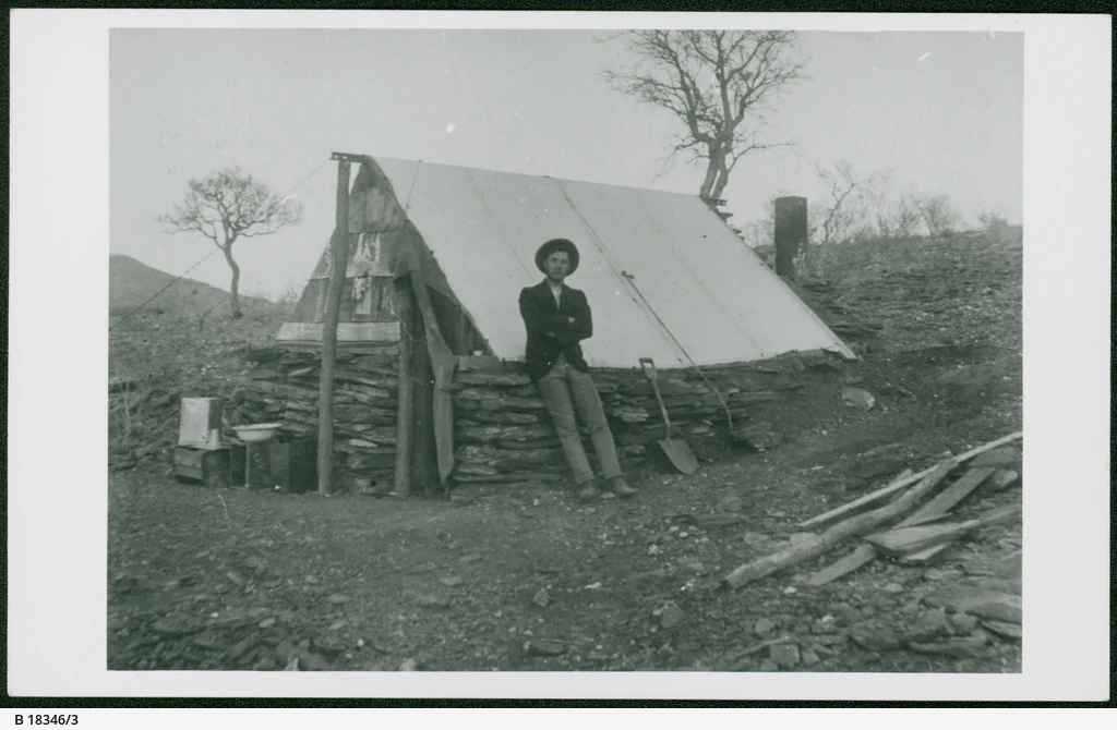 Black and white historical photograph showing a man standing in front of a small tent and stone structure at Arltunga in the late 19th century.