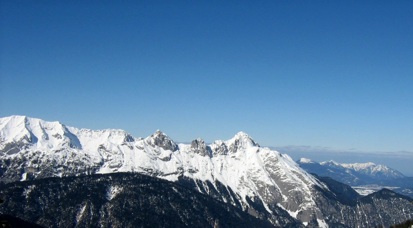 A wide, clear-day panoramic view of the rocky, snow-dusted Arnspitze Group mountain range under a deep blue sky.