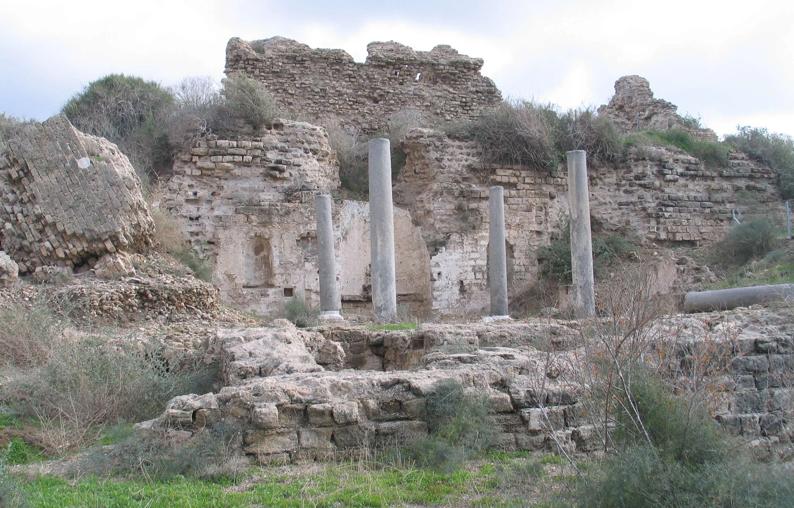 Stone columns and ancient stone ruins with scattered stones and vegetation in a coastal area
