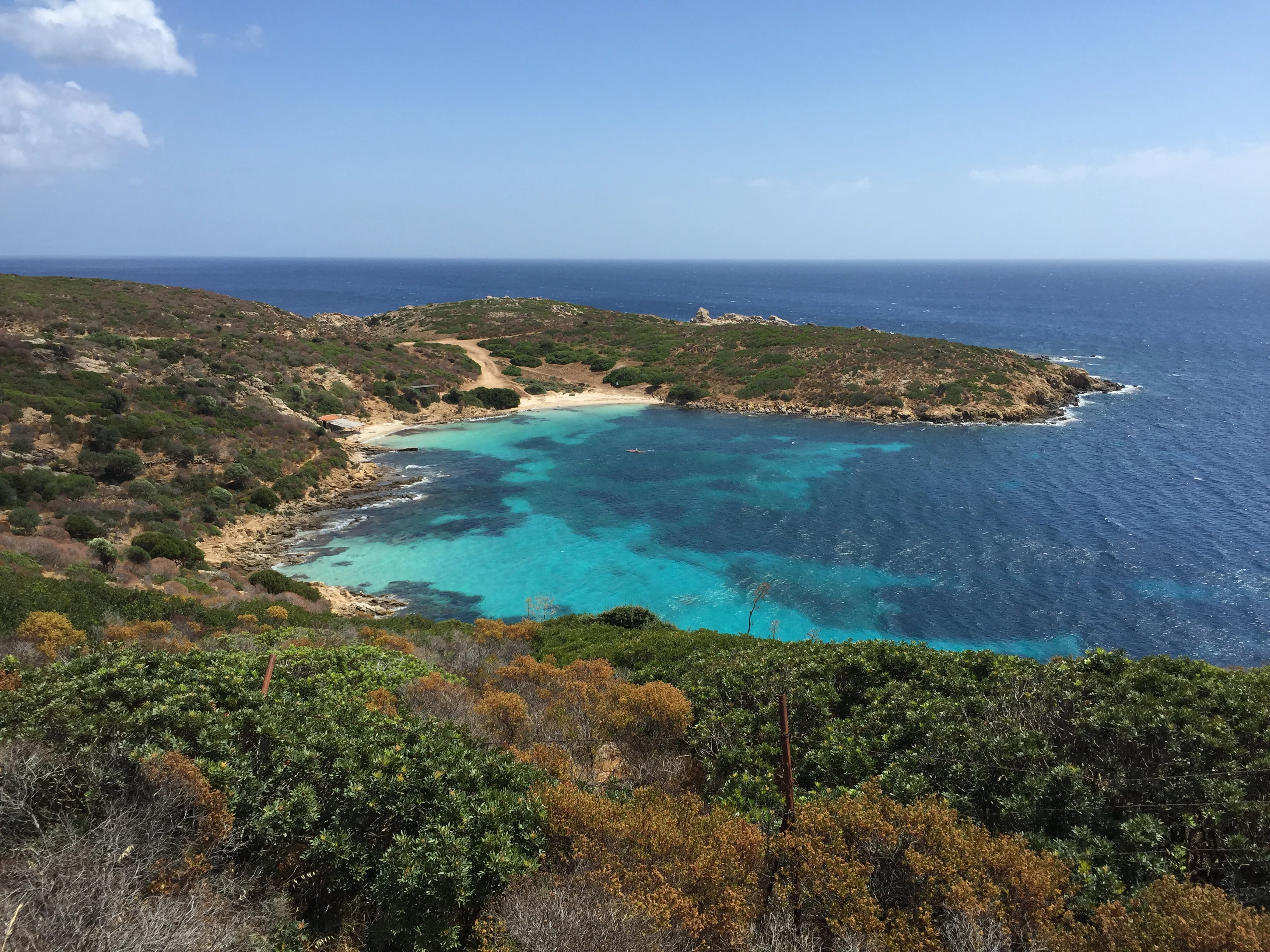 Panoramic view of Cala Sabina beach featuring turquoise water, sandy shore, coastal cliffs, and lush green vegetation under a clear blue sky.