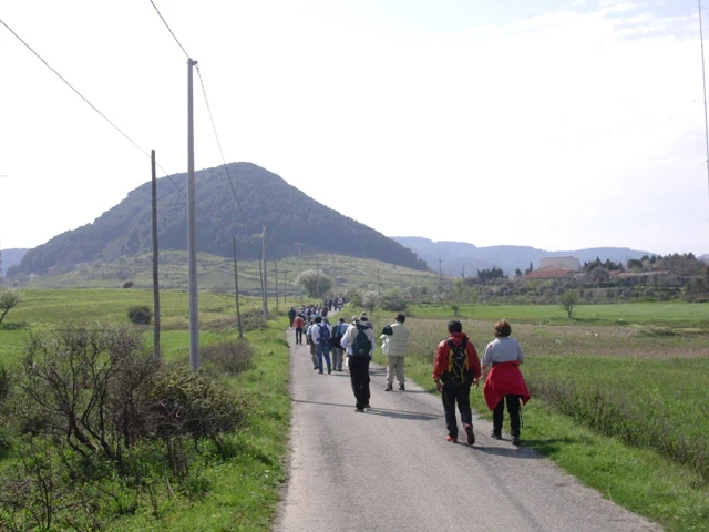 Group of hikers walking on a paved road through a rural landscape with a mountain in the background