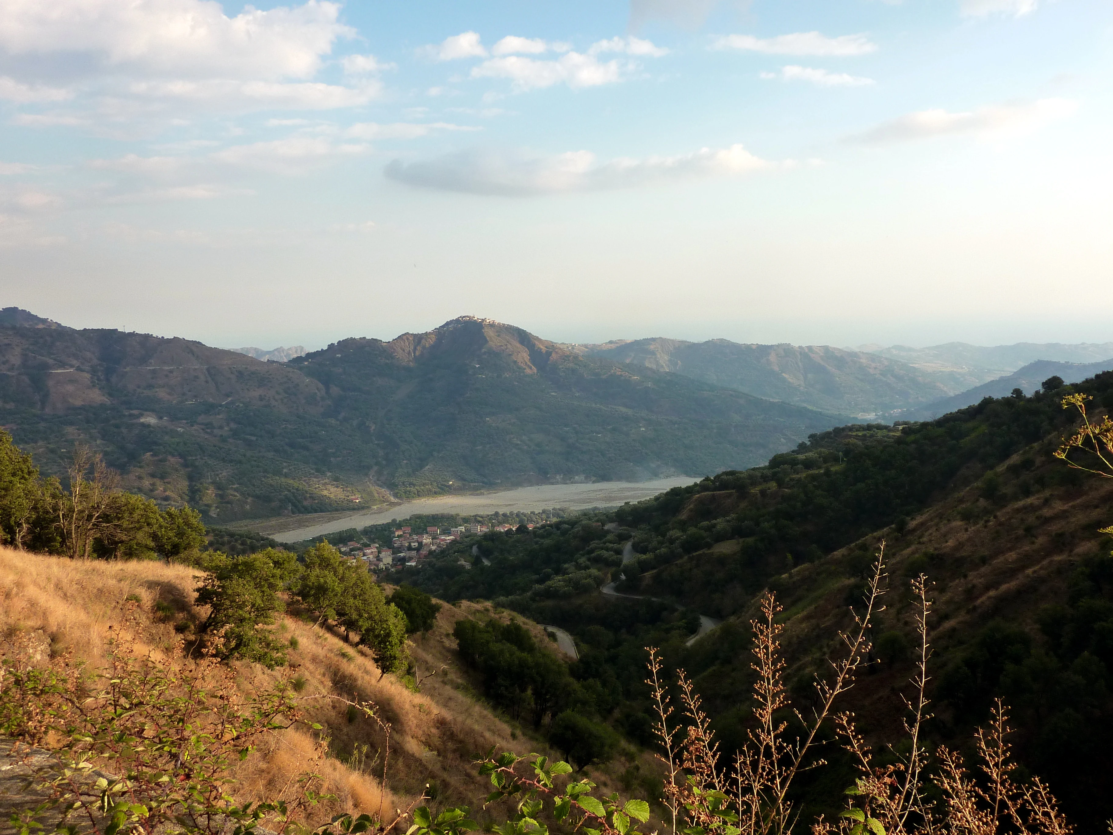 Mountainous landscape in Aspromonte National Park with dry grass, hills, and distant mountains under a partly cloudy sky
