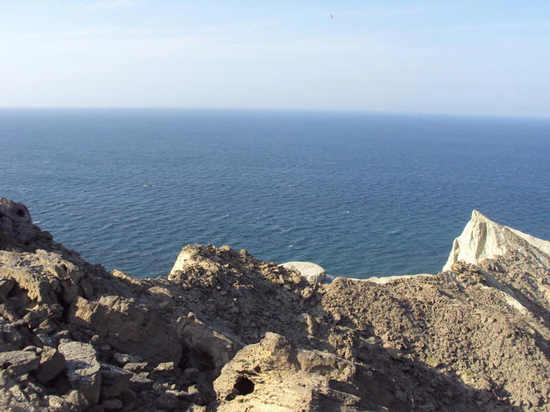 A high angle view looking down from rocky cliffs on Astola Island toward the deep blue waters of the Arabian Sea.