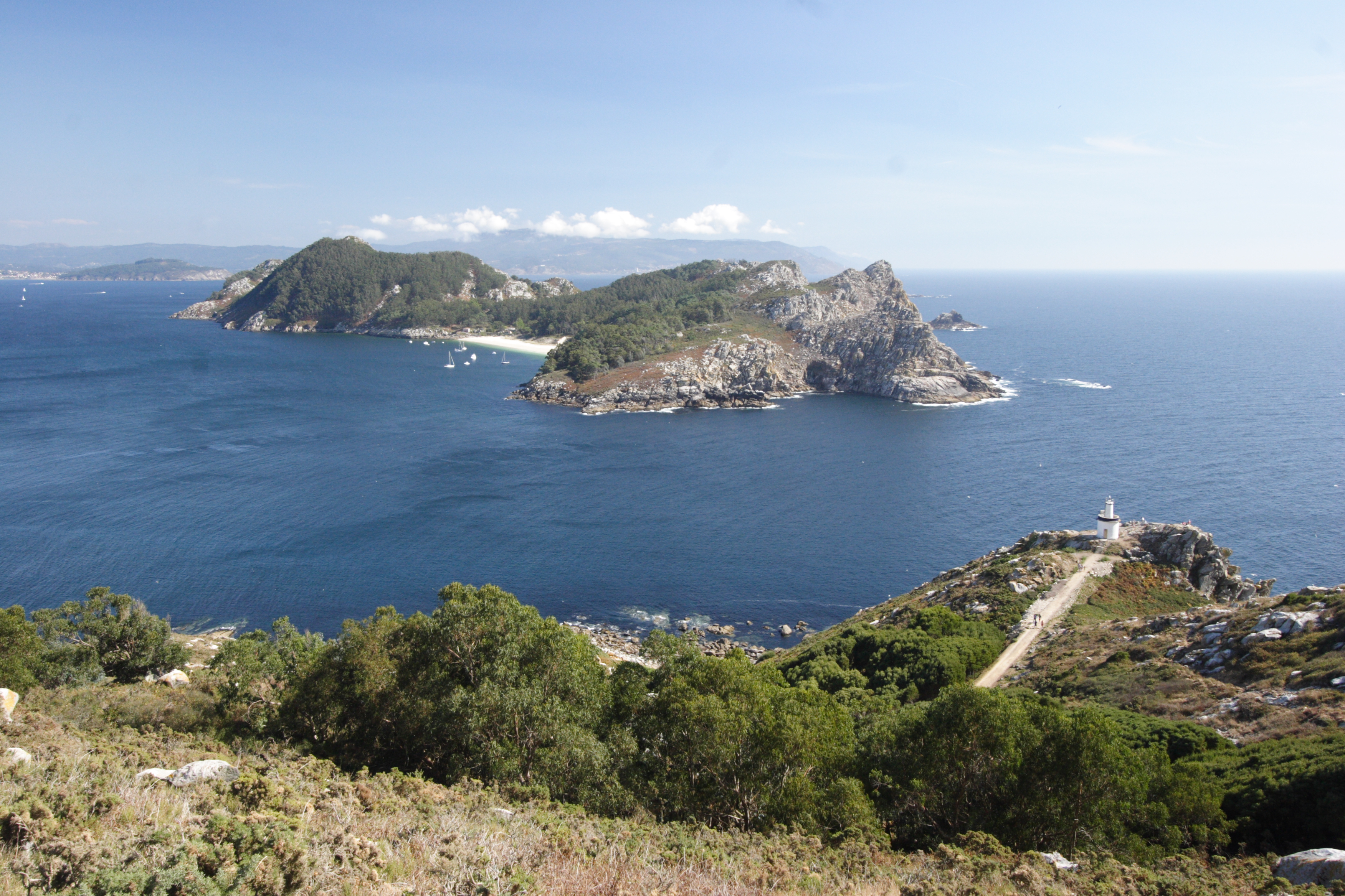 Panoramic coastal view showing the Cíes Islands in the distance with green hills and blue water in the foreground