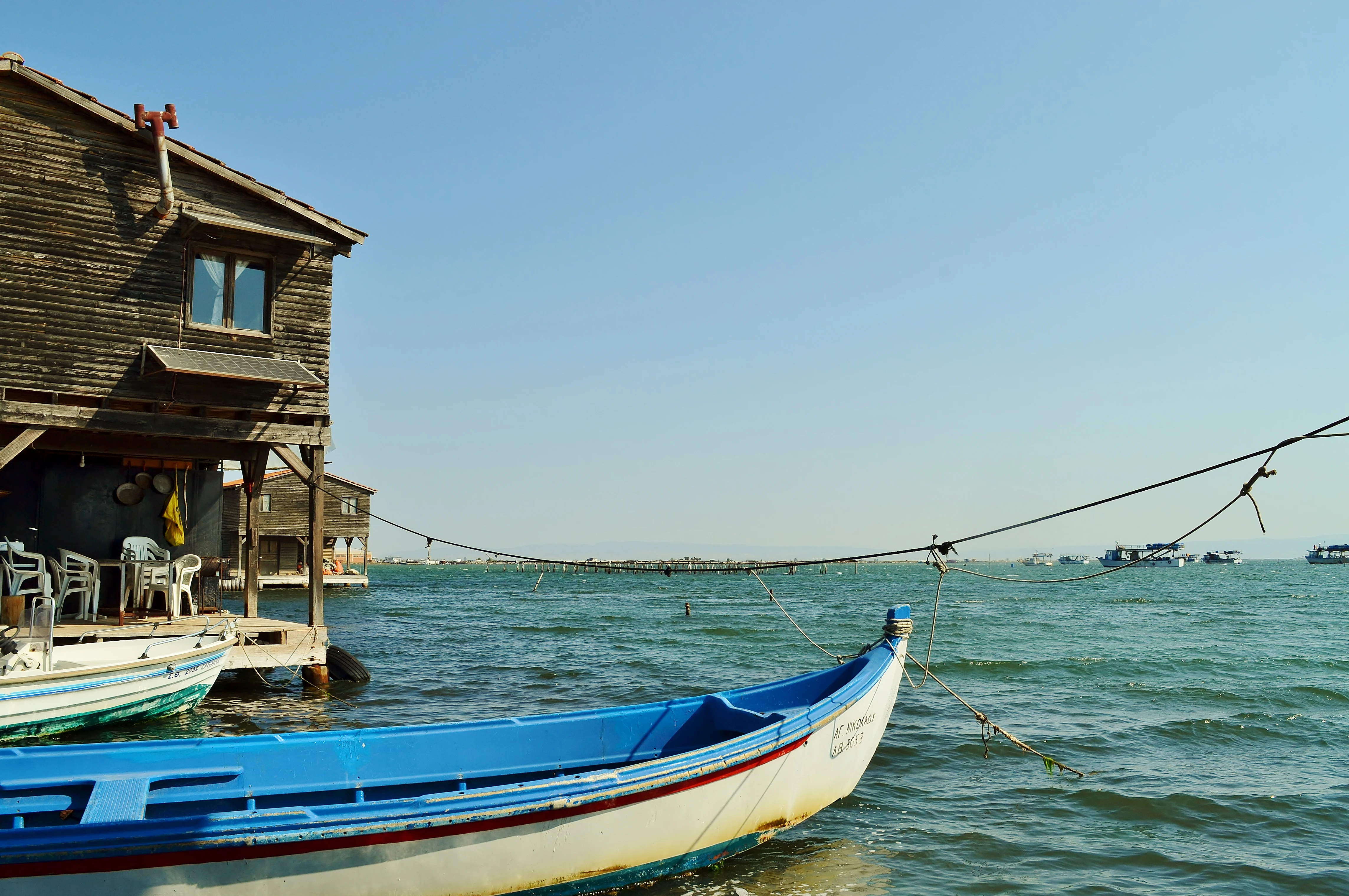Blue and white fishing boat docked next to a wooden stilt house on water with open sea in background