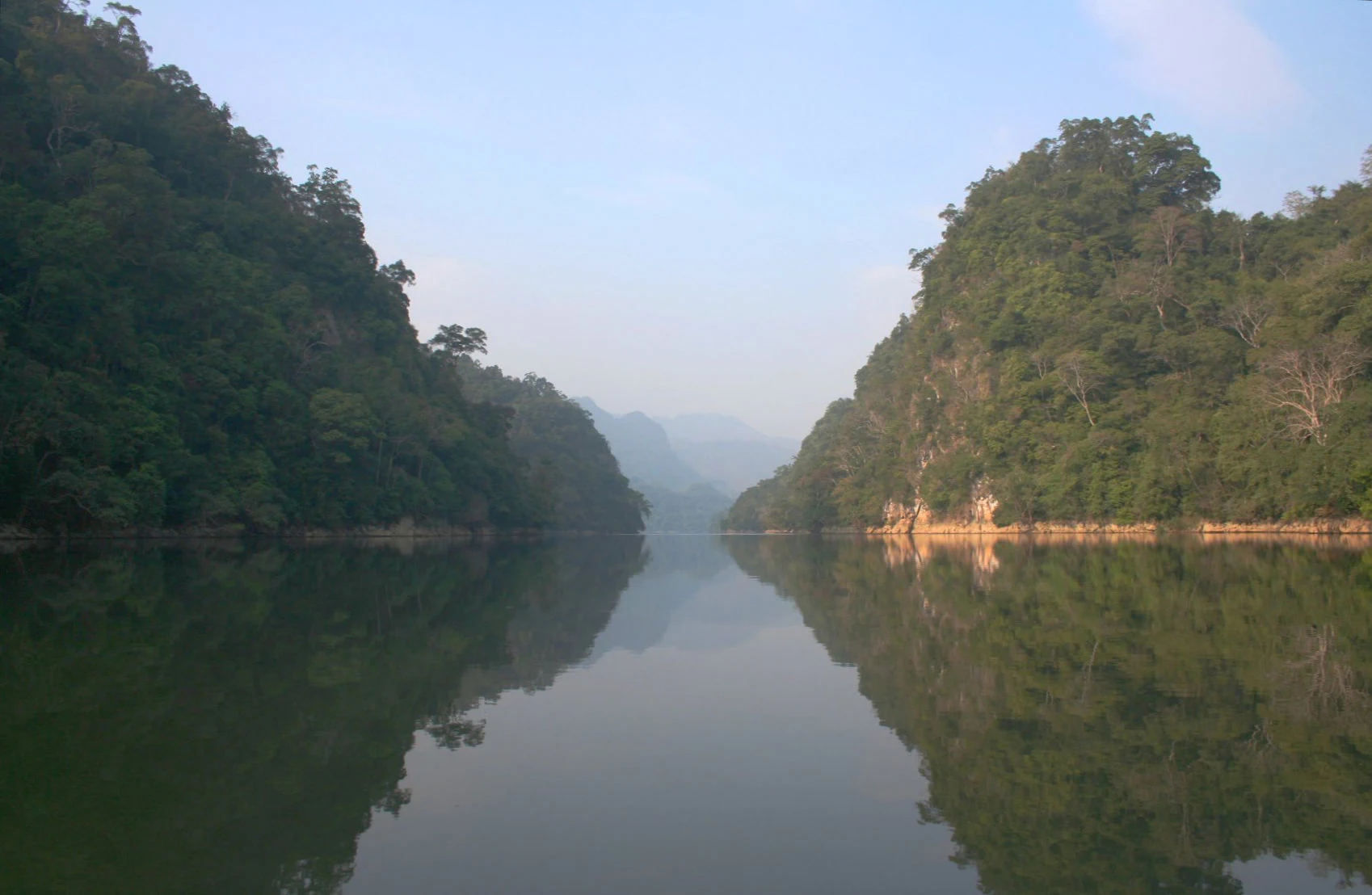 Calm lake reflecting dense forested hills under a clear sky