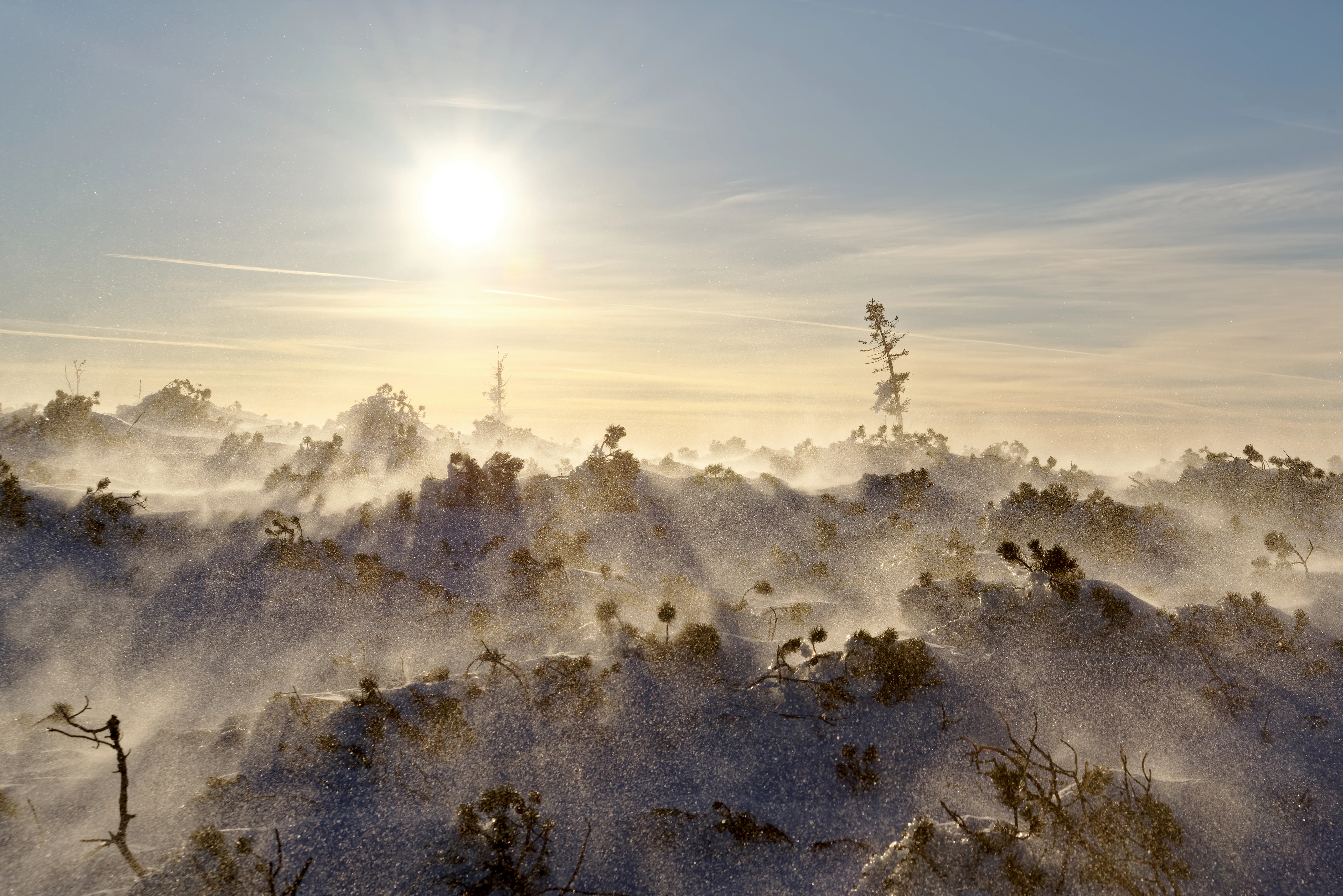 Snow-covered mountain slope with blowing snow and crepuscular rays from the sun in early morning