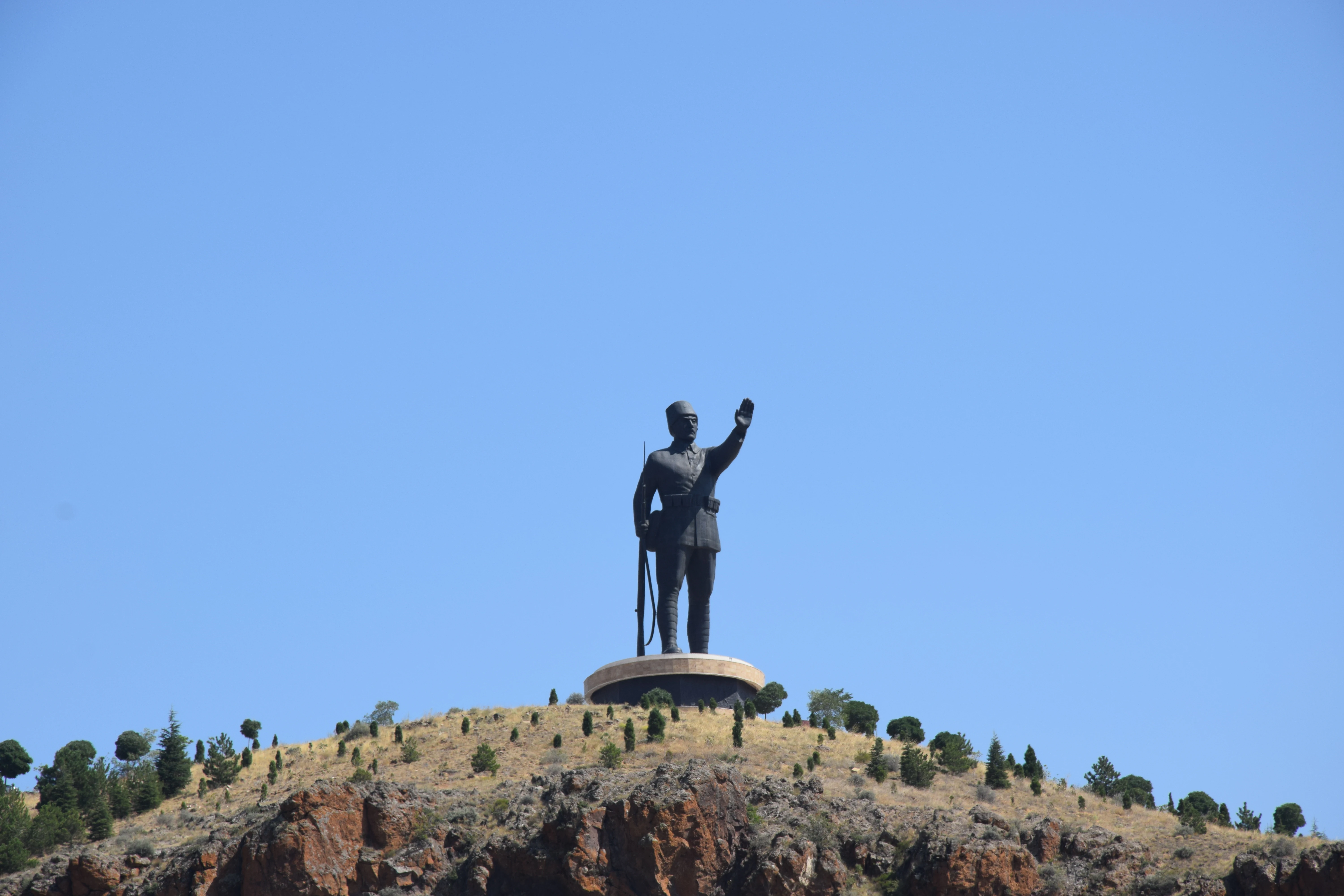 Large statue of a person standing on a hilltop with a clear blue sky background
