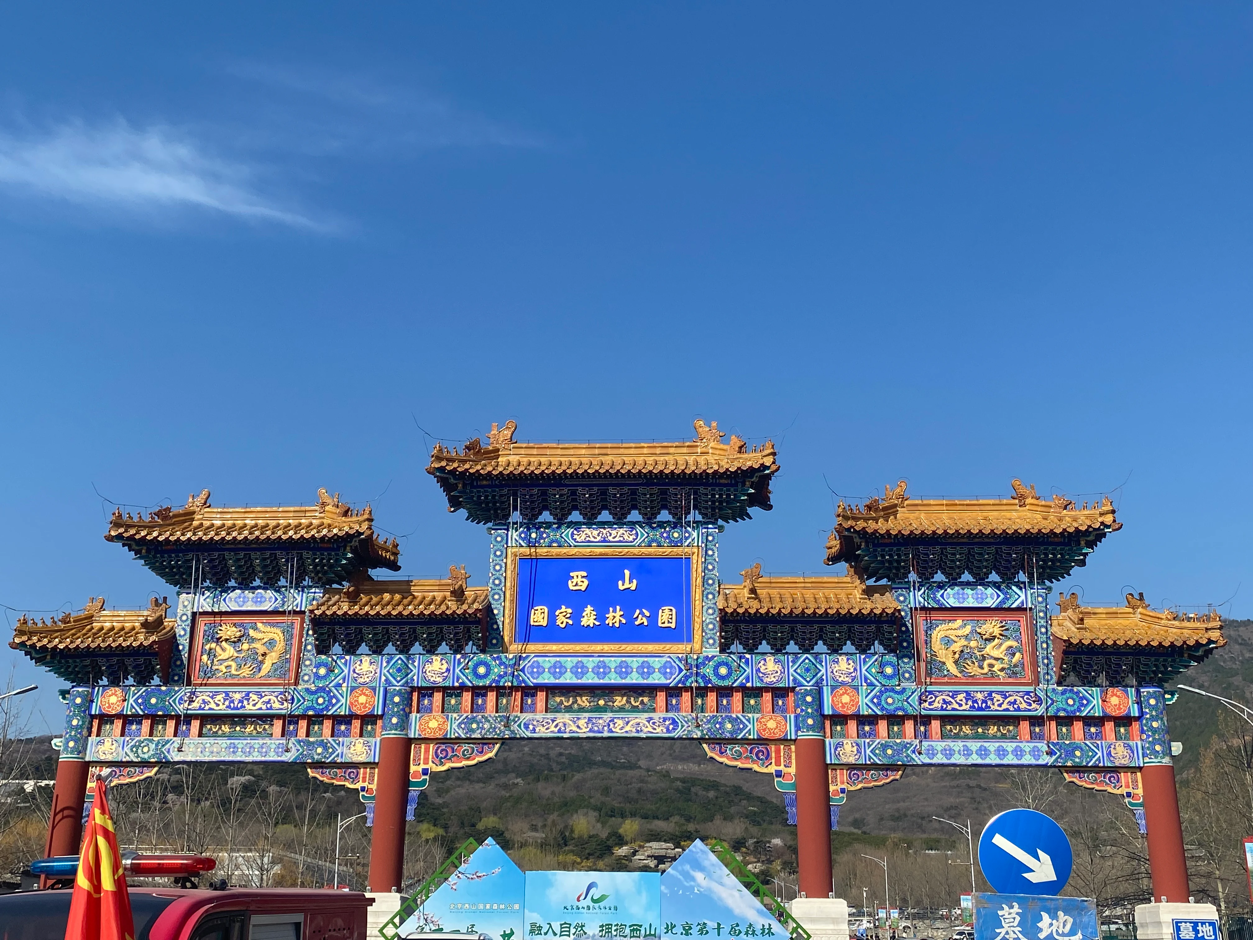 Una gran puerta ornamentada de estilo tradicional chino, con techos dorados e intrincados patrones azules y rojos contra un cielo azul despejado, que sirve como entrada al parque.