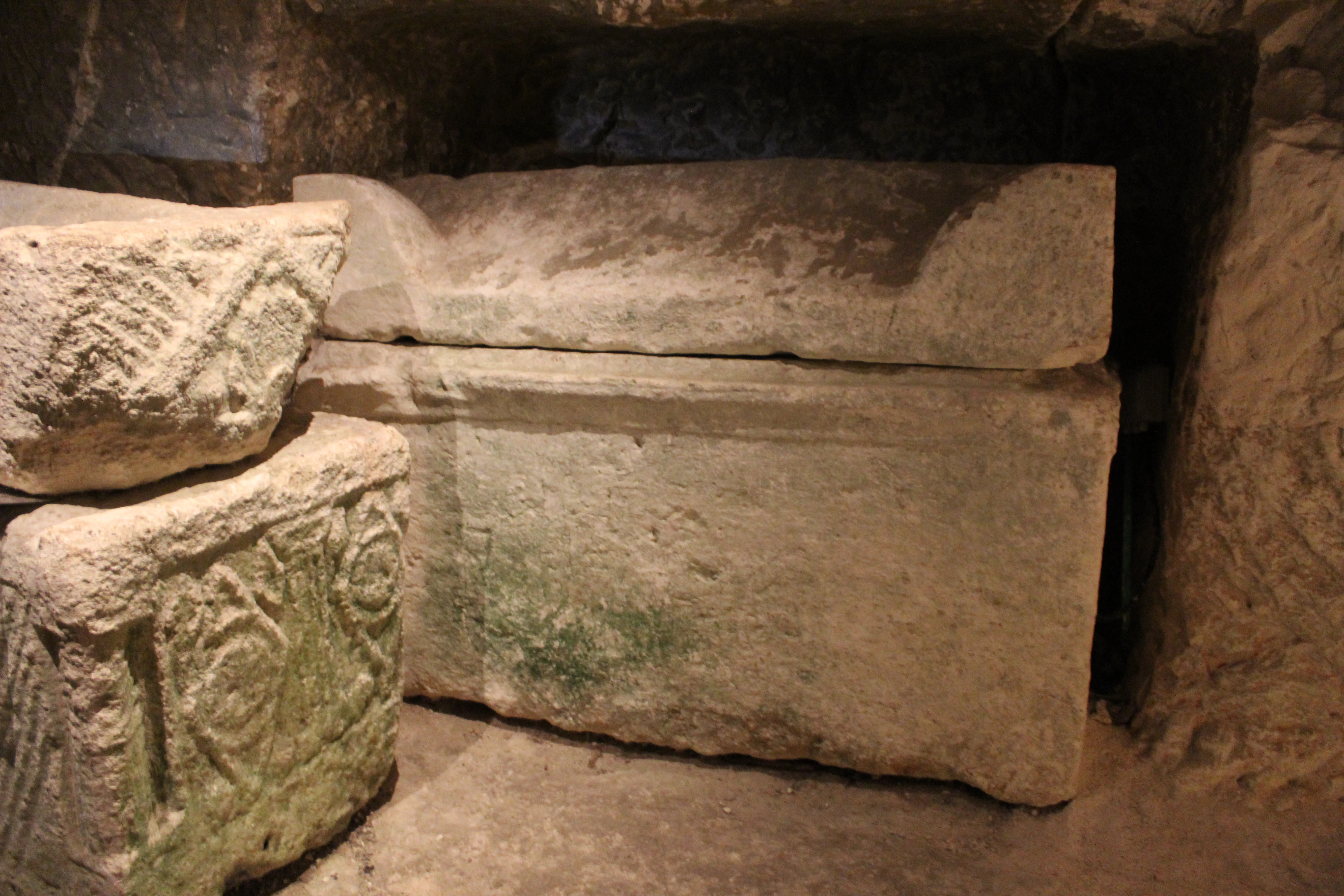 Ancient stone sarcophagi with carvings inside a narrow catacomb passage