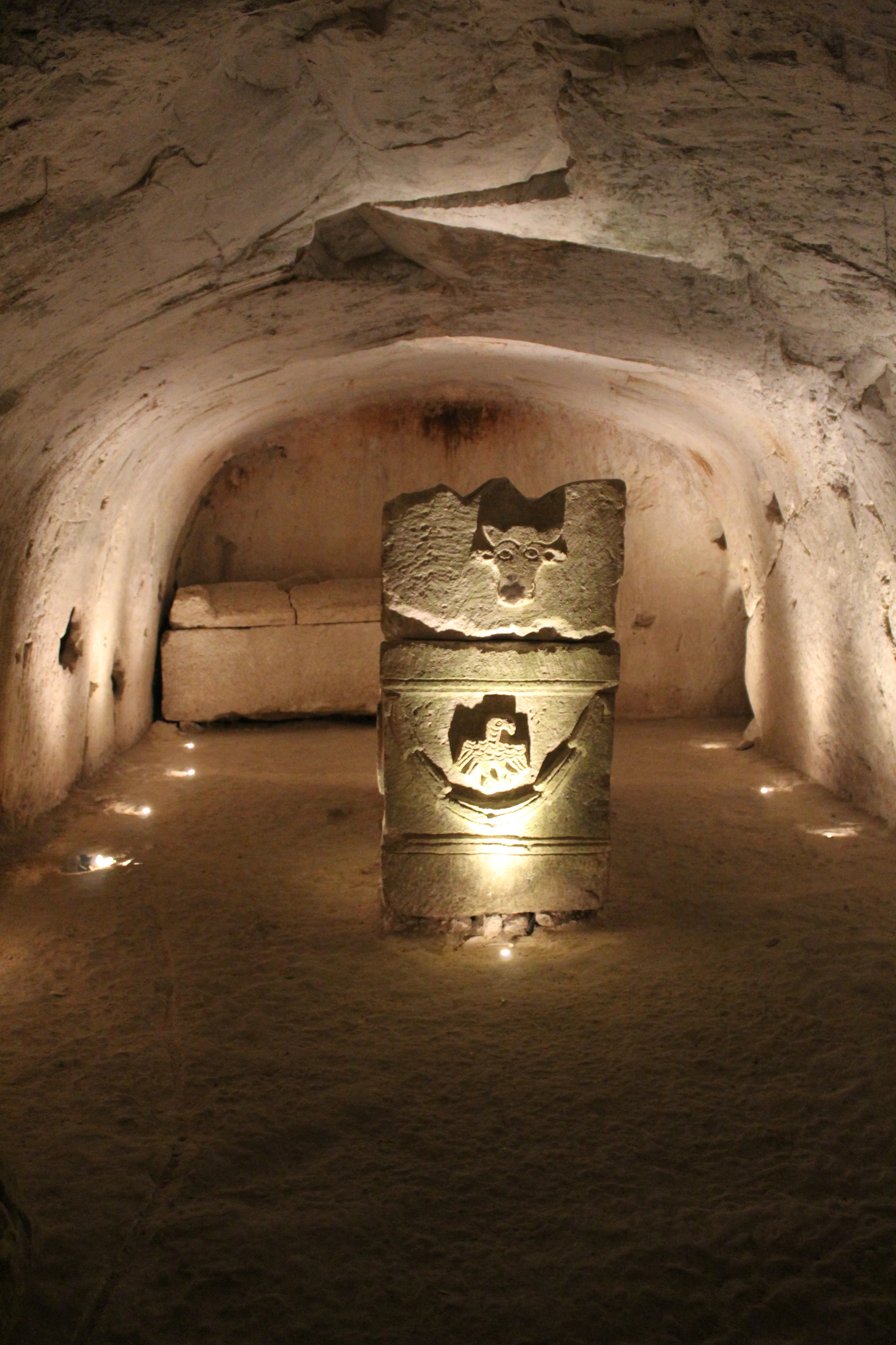 Stone sarcophagus with decorative carvings illuminated by small lights inside an underground chamber with arched stone walls