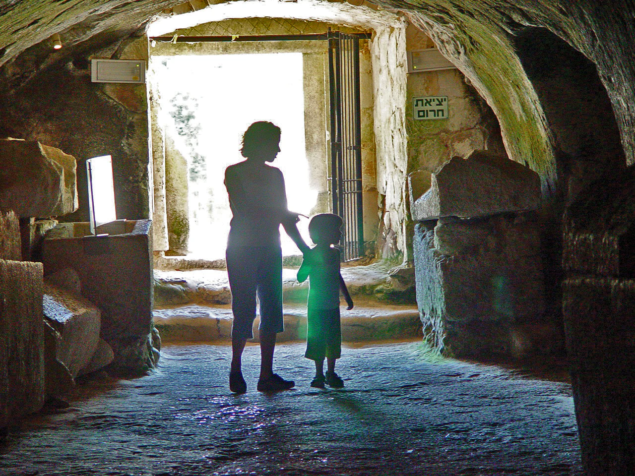 Silhouettes of an adult and child holding hands inside a stone tunnel with bright light visible at the exit