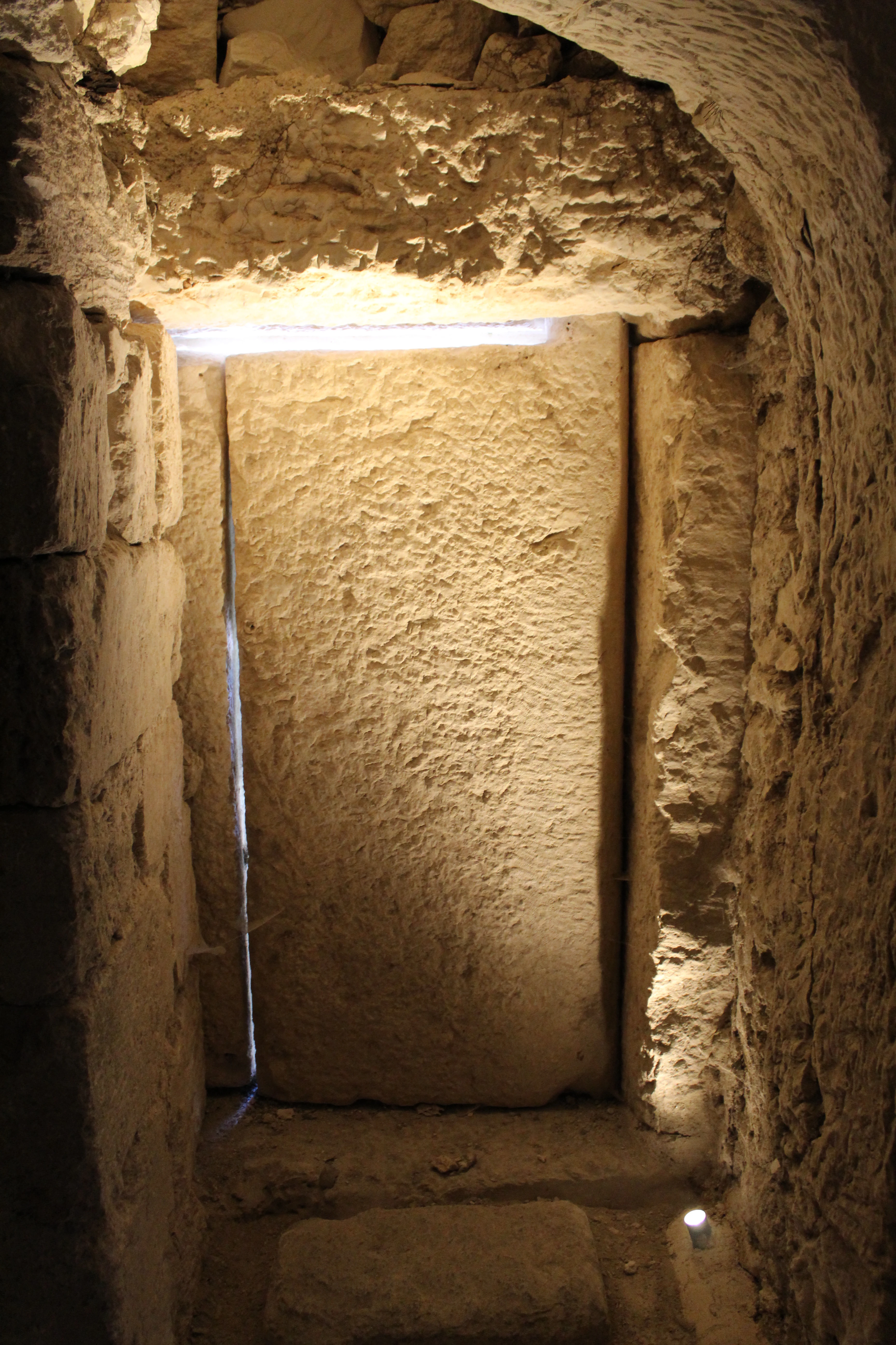 Stone doorway inside ancient catacomb with rough stone walls and artificial lighting