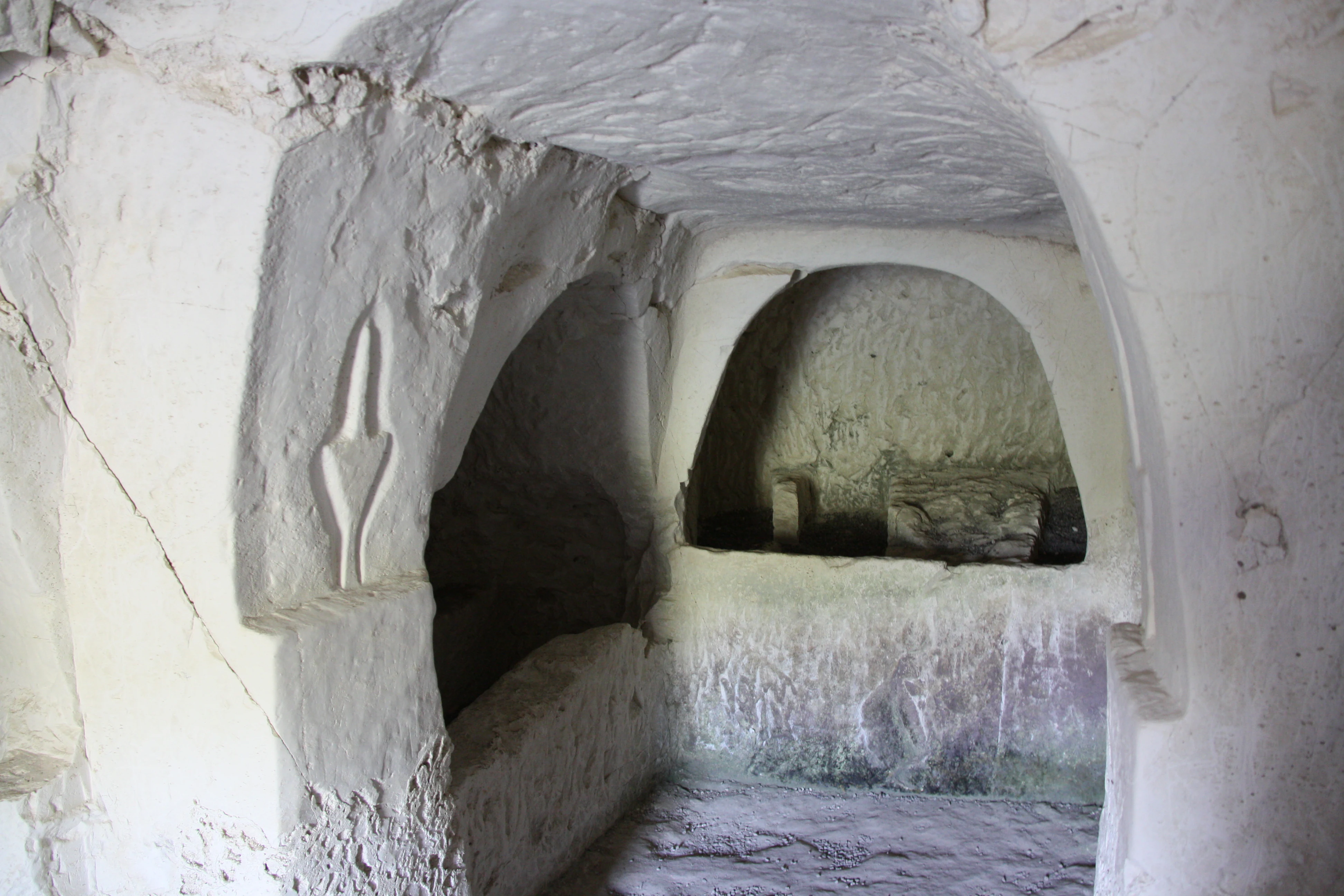 Stone-carved burial chamber interior with vaulted ceiling, niche shelves, and carved stone element on left wall
