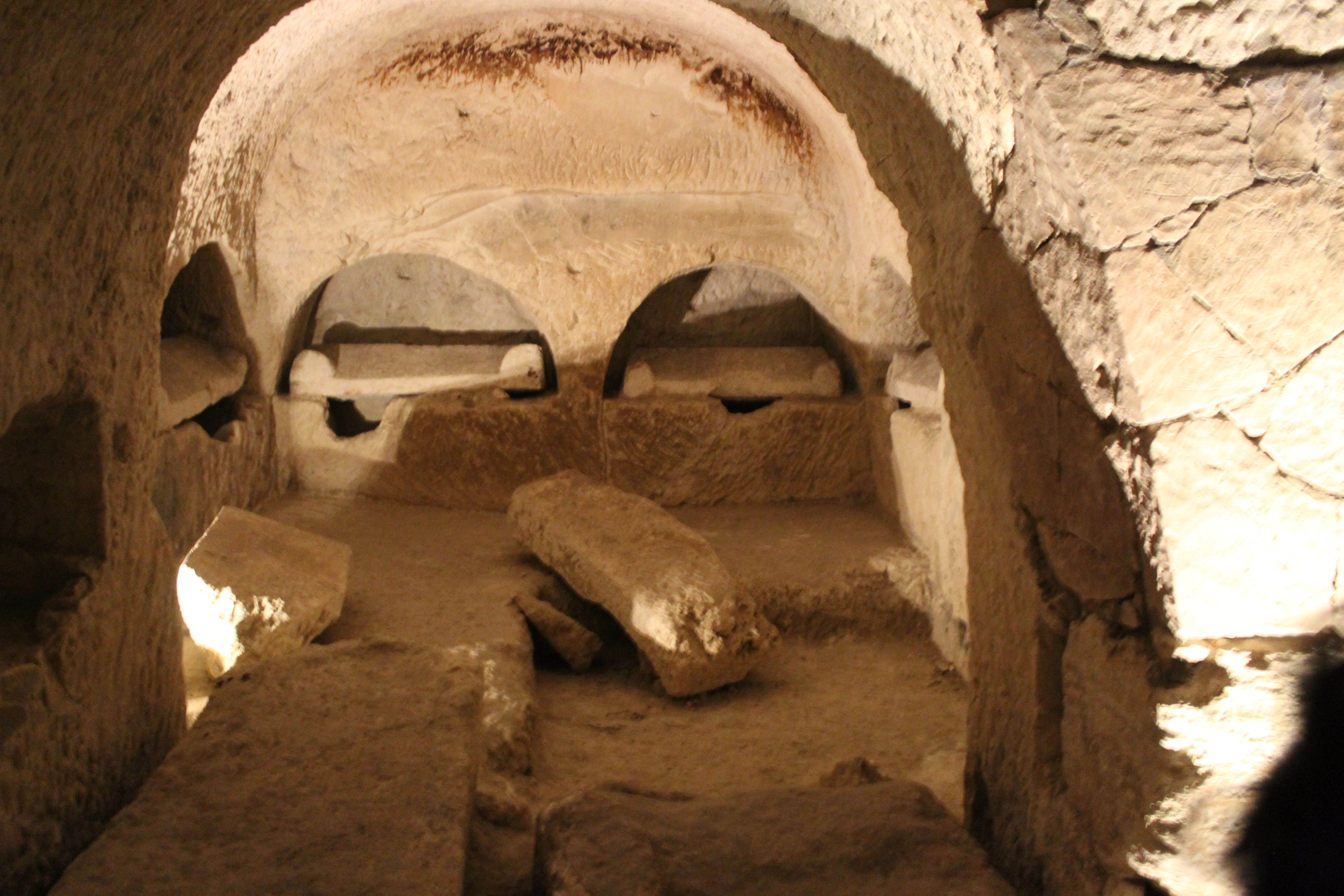Stone burial niches carved into the walls of an ancient chamber with arched ceiling and scattered stone slabs