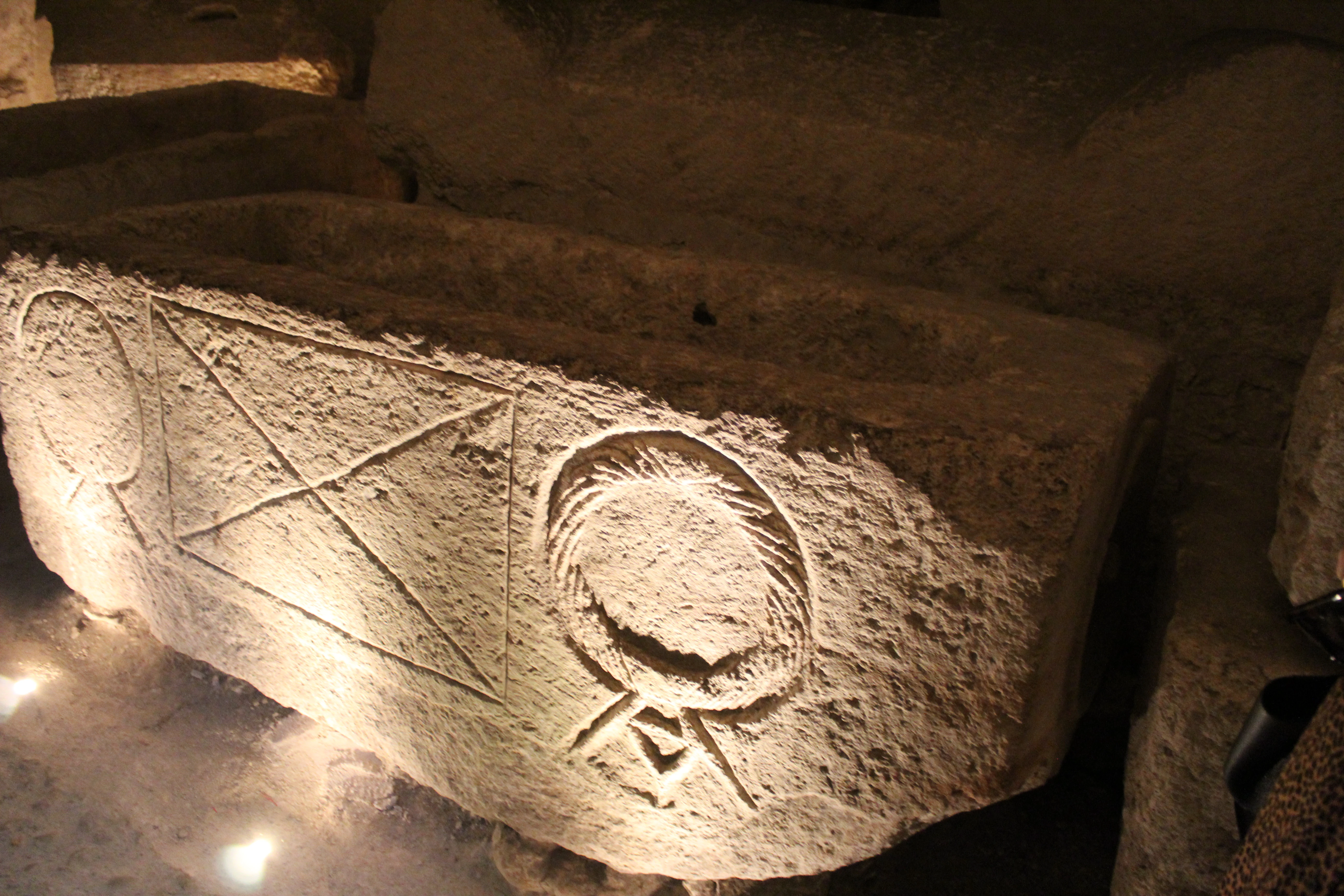 Stone sarcophagus with carved symbols inside a cave-like structure with artificial lighting