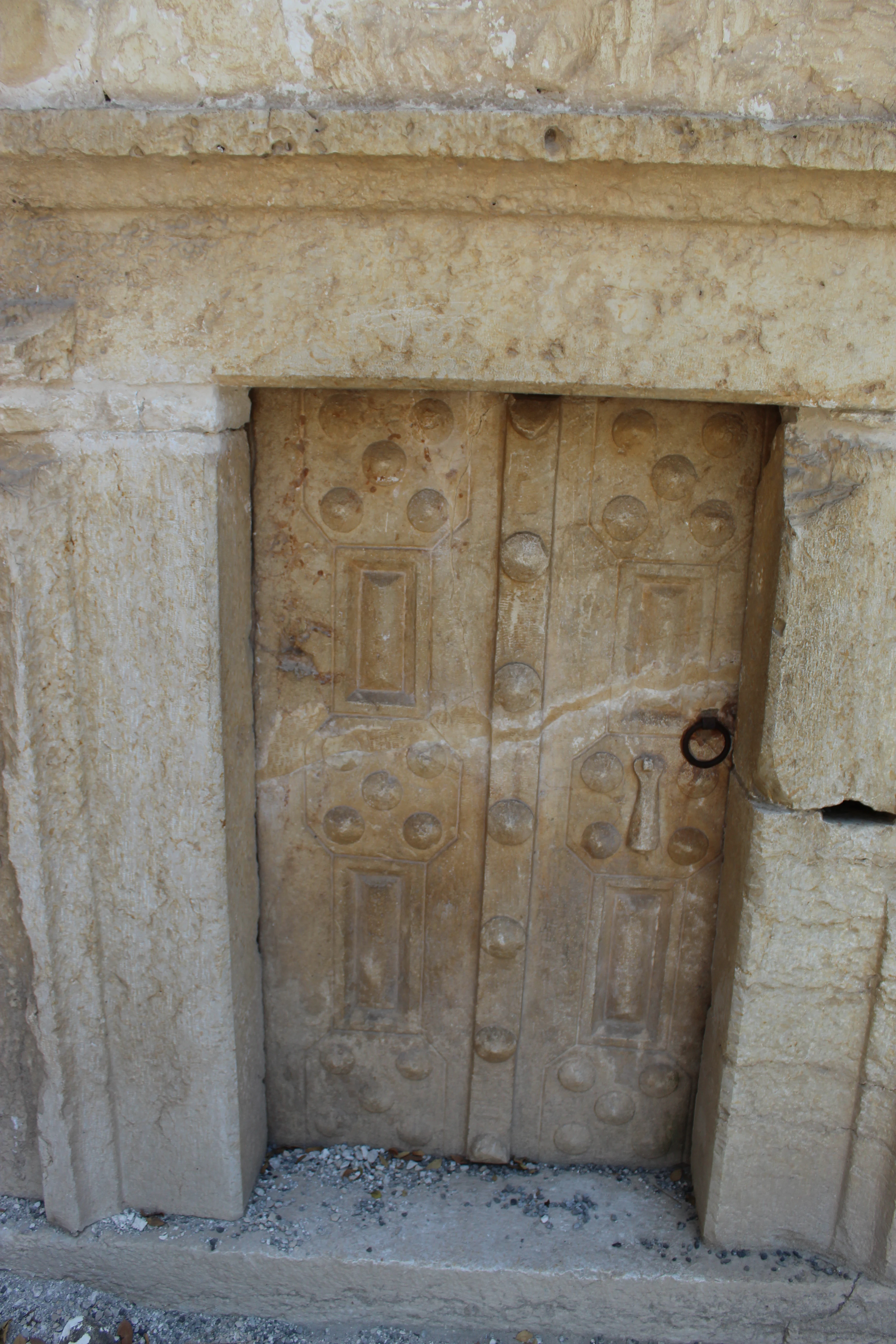 Stone door with embossed patterns including round knobs and rectangular panels set in a stone frame with a circular ring handle