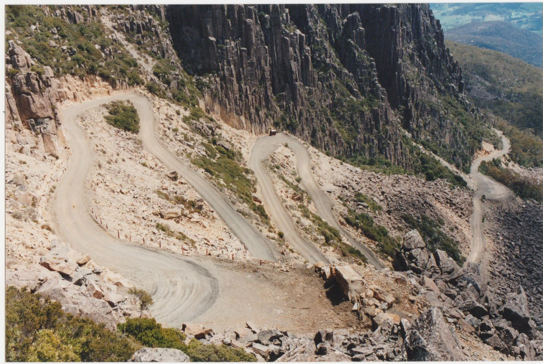 Un camino de tierra sinuoso serpentea por la ladera de una montaña rocosa con acantilados escarpados y vegetación escasa