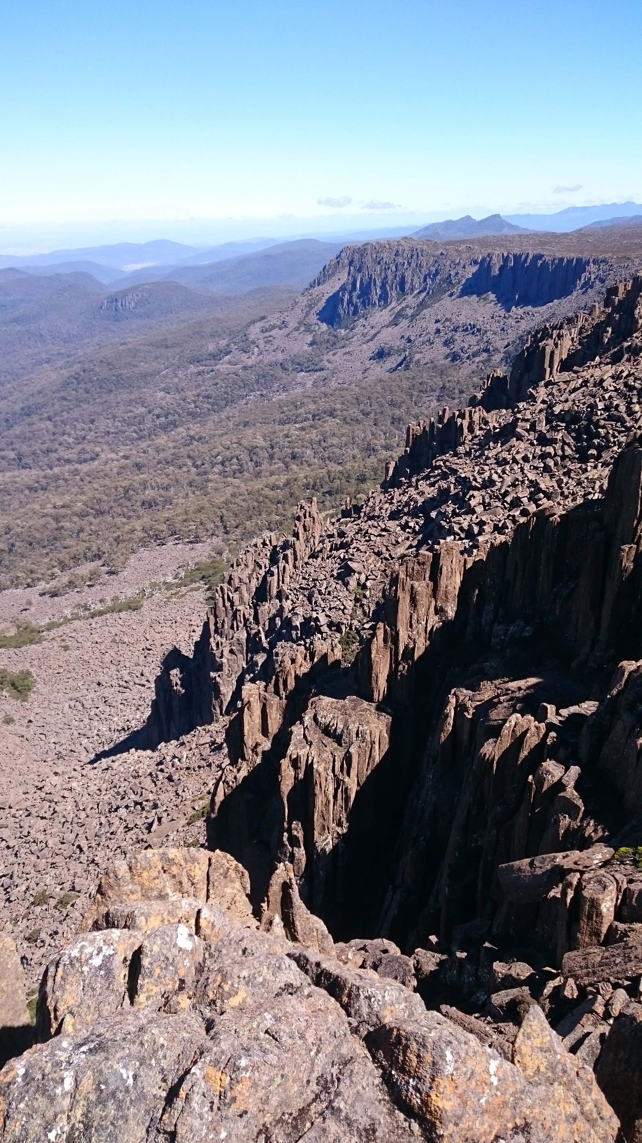 Pared rocosa con acantilados escarpados y vista al valle bajo un cielo azul claro