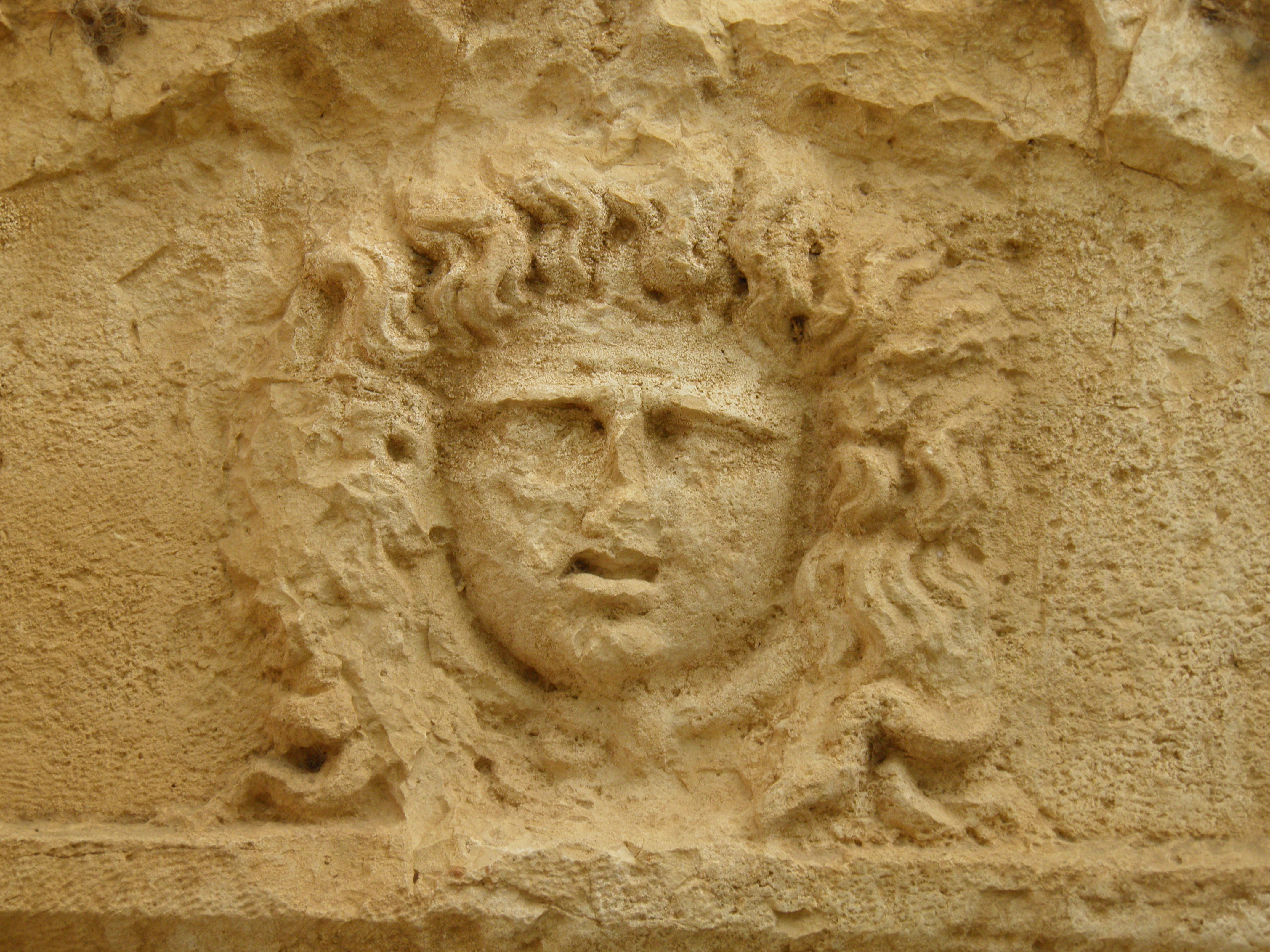 Stone relief sculpture of a human face with curly hair on a weathered stone surface