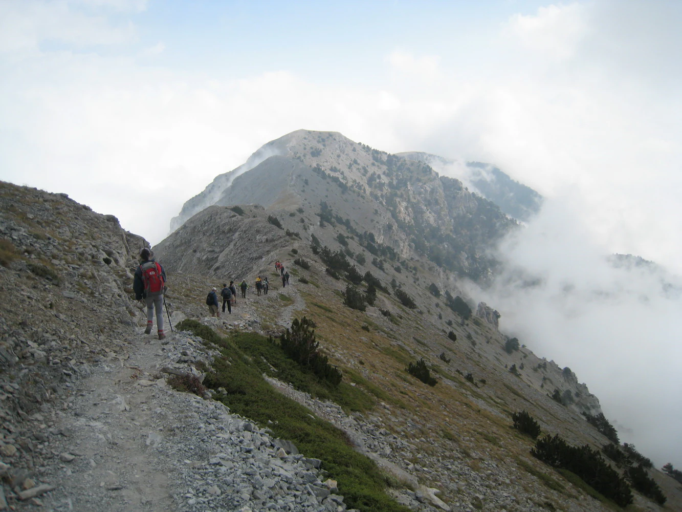 Hikers on a rocky trail with a mountain peak in the background, partially obscured by clouds.